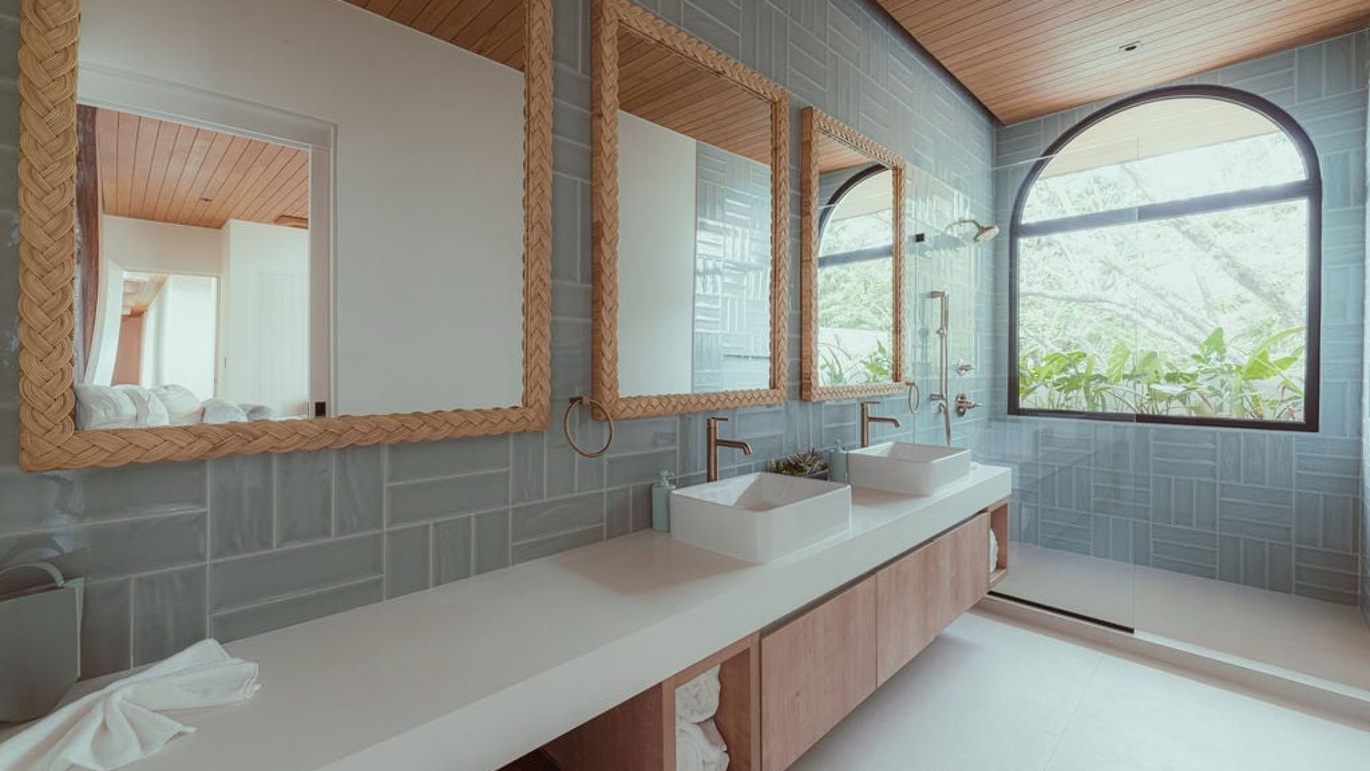 Natural wood-framed mirrors in a bright modern bathroom with large window and double sinks.
