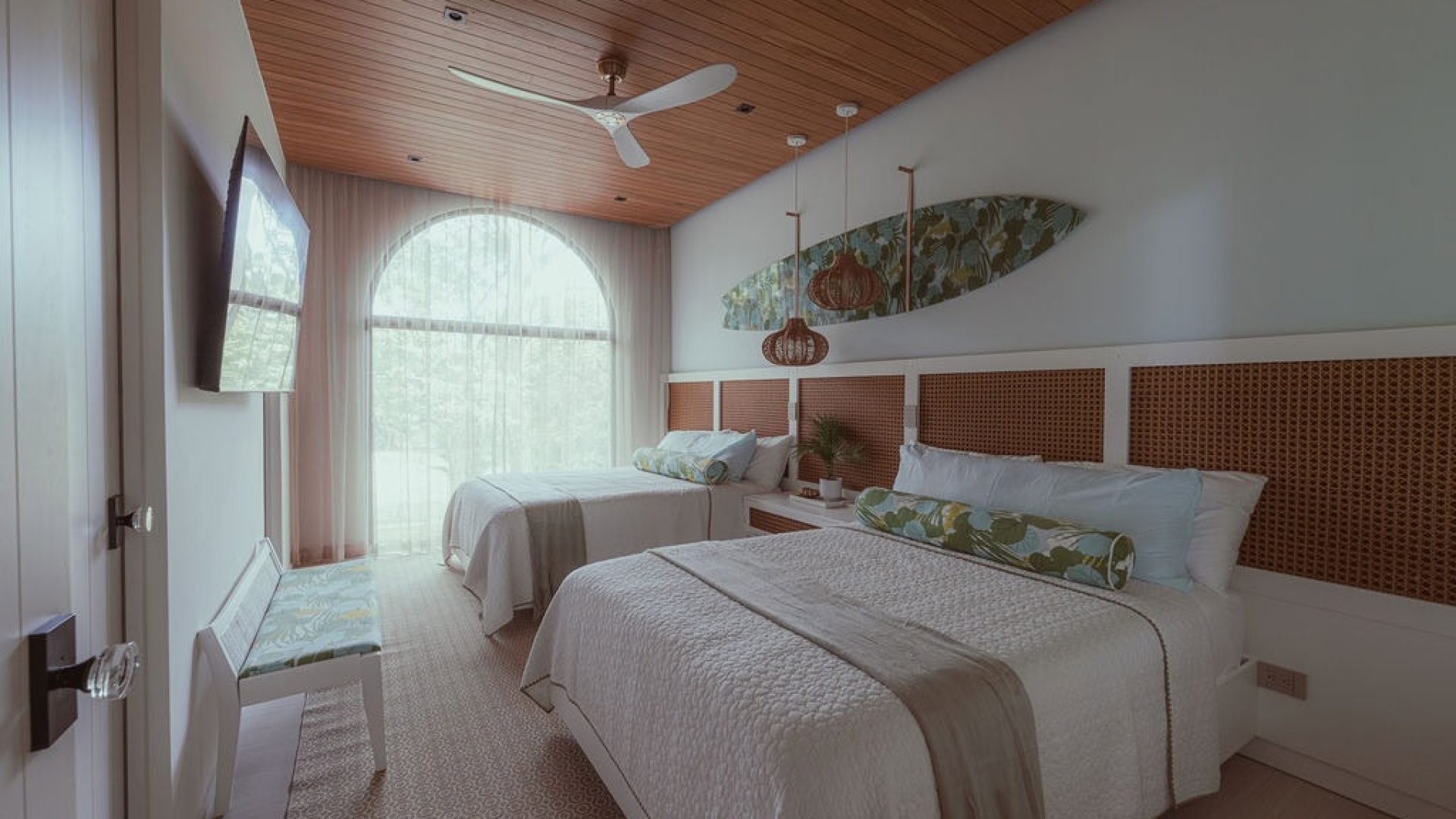 Bright hotel room with large arched window and tropical decor accents.
