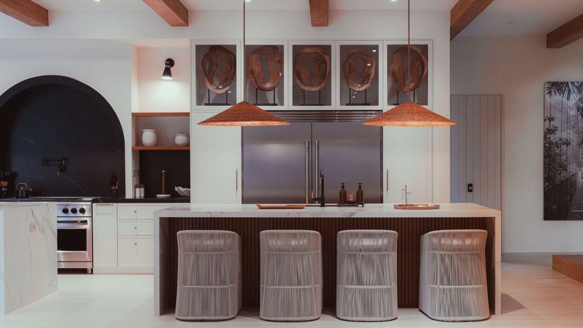 Modern kitchen with marble accents and stylish bar stools, featuring contemporary decor and warm wooden ceiling beams.