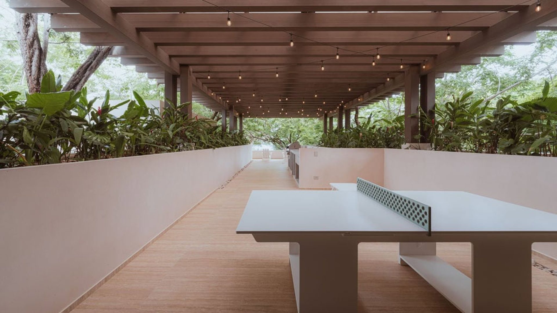 Modern outdoor ping pong table under a wooden pergola surrounded by lush greenery for Vida Pinilla.