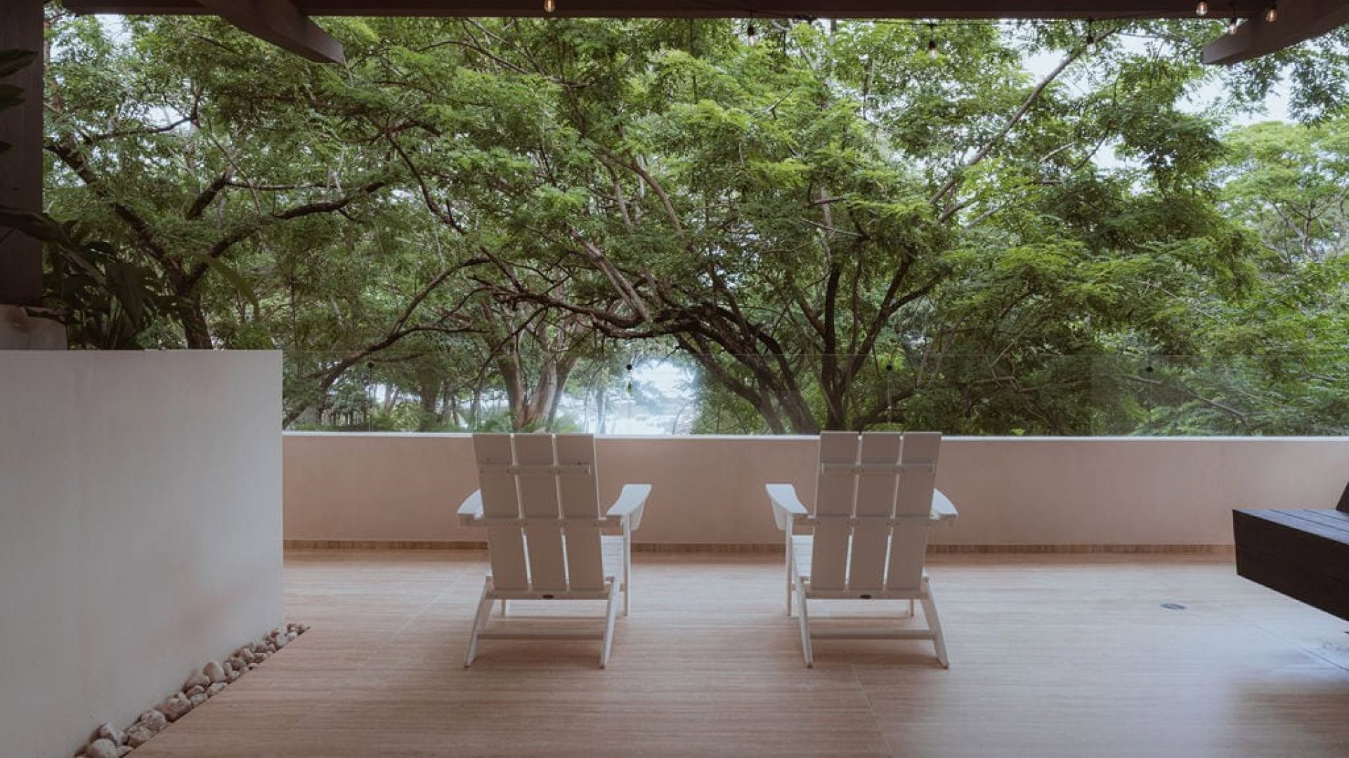 Serene balcony with lush green trees, modern white lounge chairs, and tranquil outdoor vibe for relaxation.