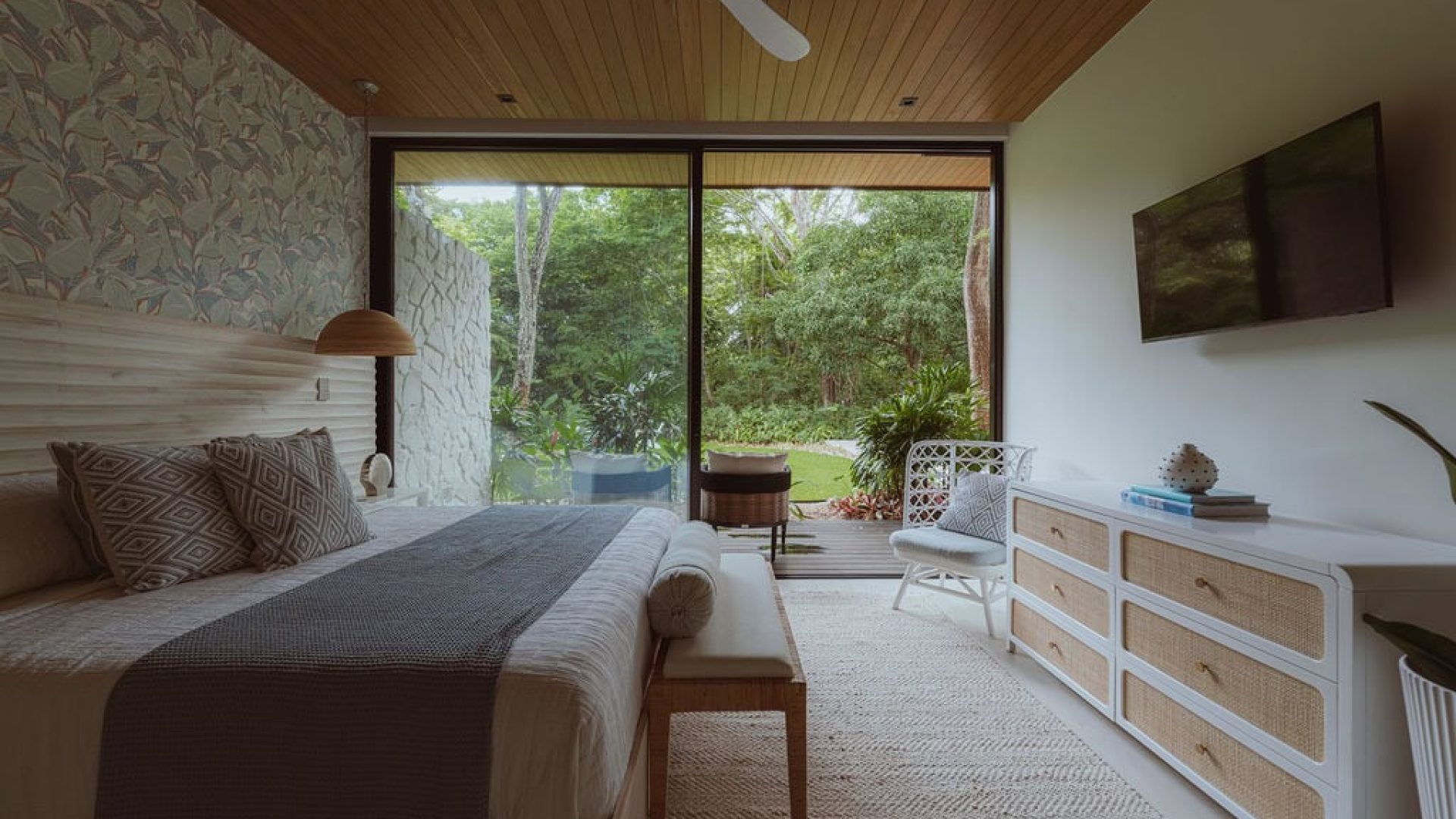 Cozy bedroom with large glass door opening to lush green garden, natural wood accents, and modern decor.