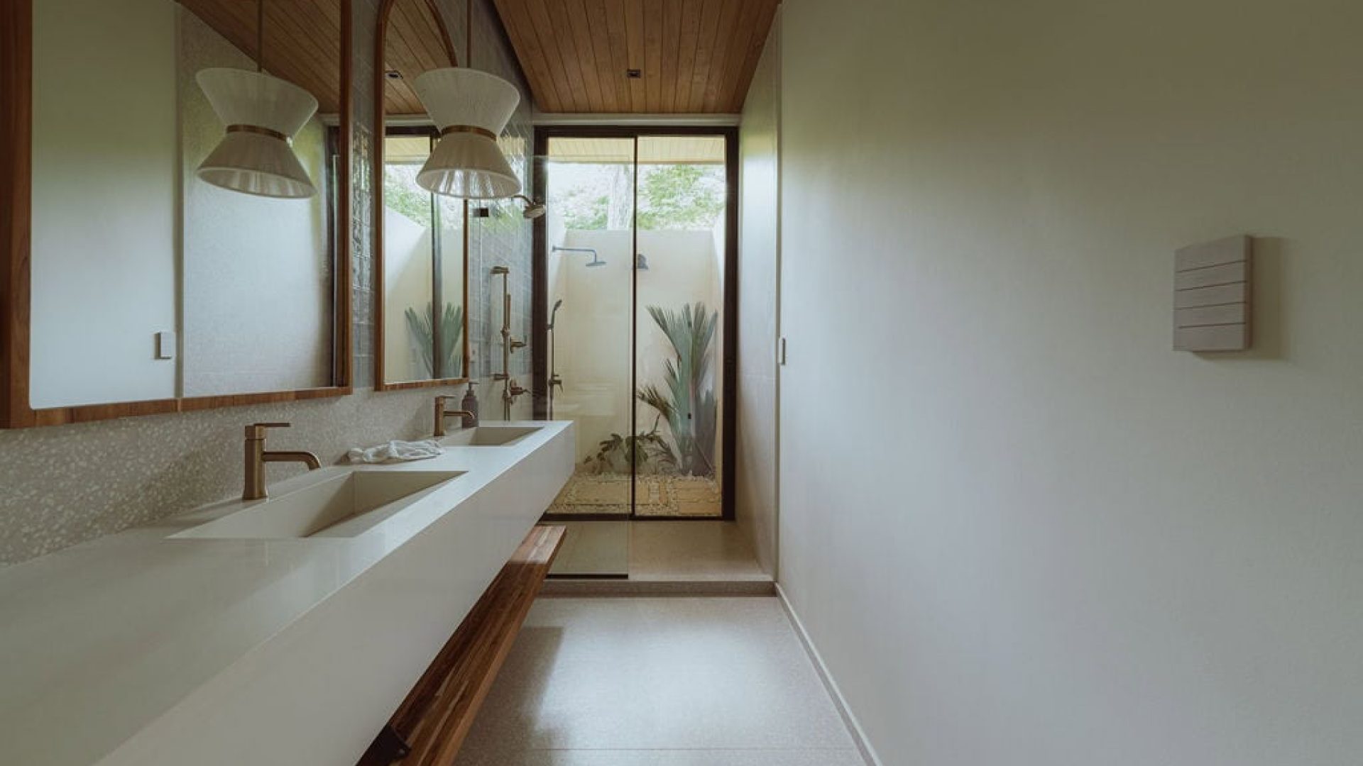 Modern bathroom with double sinks and wooden accents, bright natural light, and tropical garden view.