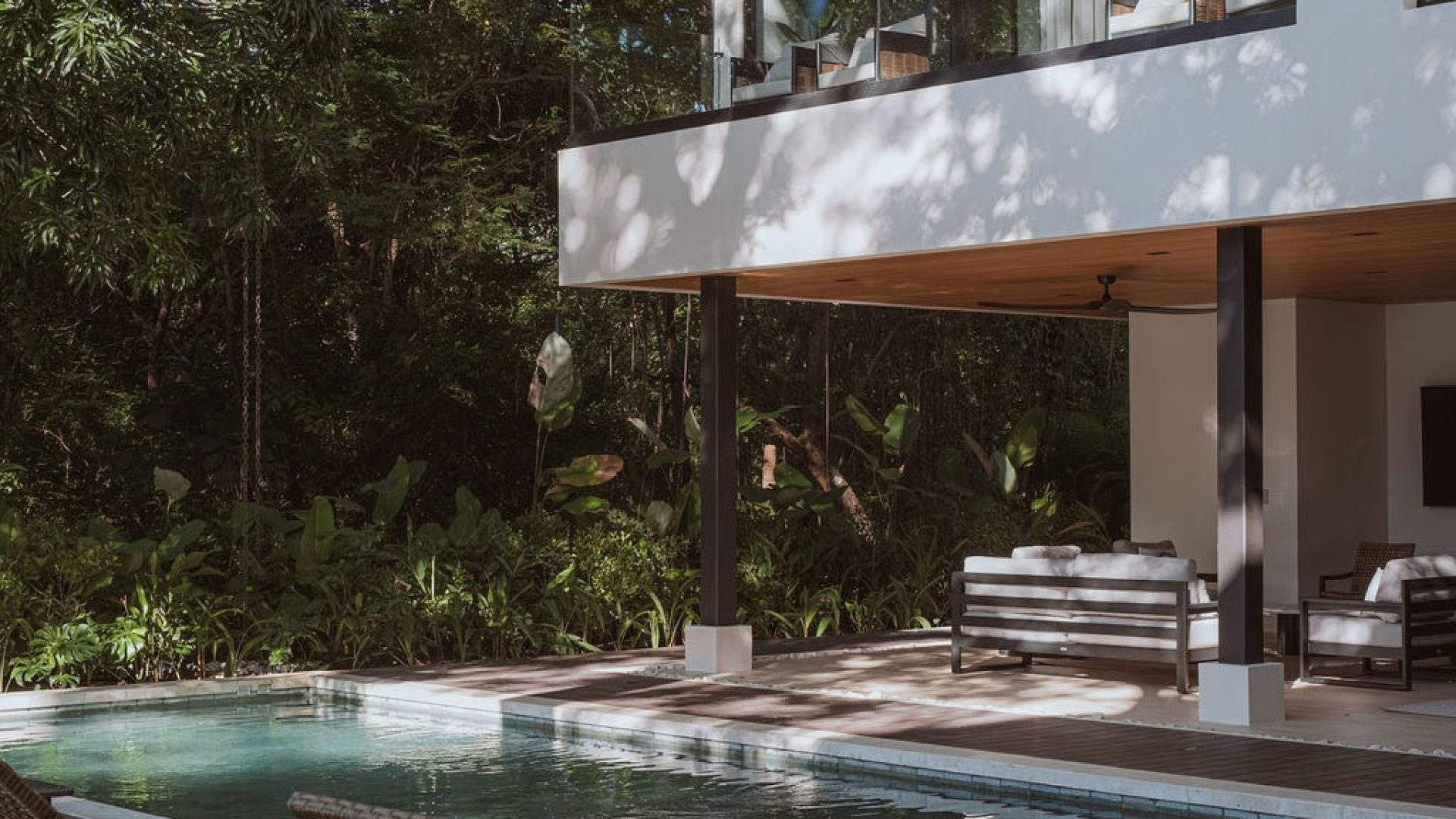 Luxurious modern house with private pool surrounded by lush greenery and outdoor seating area.