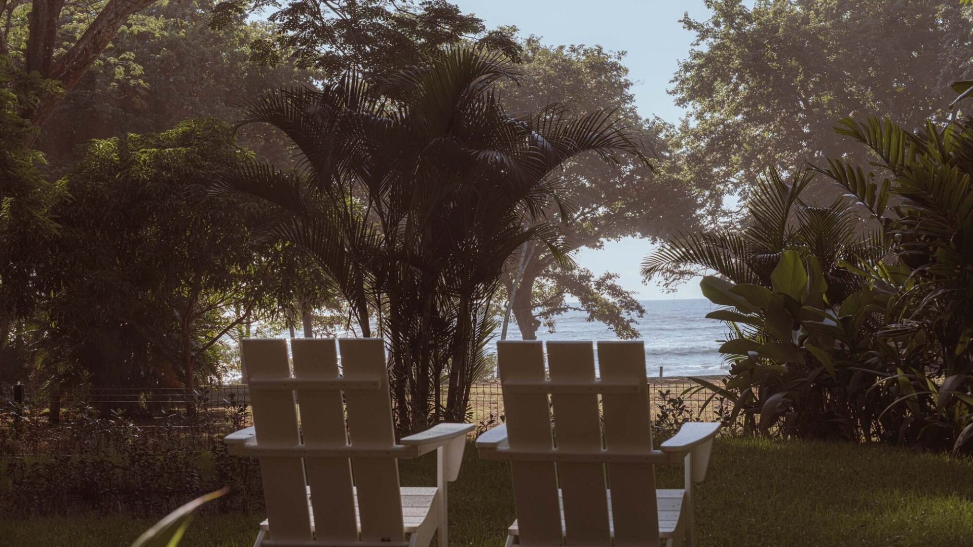 Peaceful beach view with two white chairs under lush trees, overlooking the ocean at Vida Pinilla.