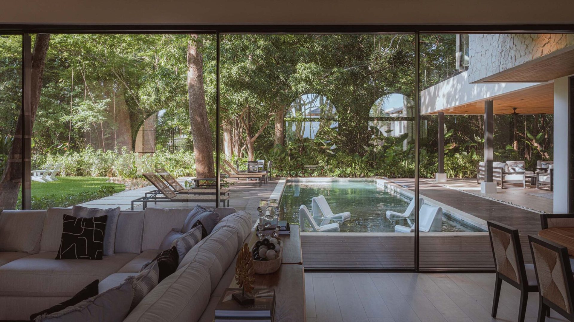 Stunning modern living room with floor-to-ceiling glass doors opening to a lush backyard with pool.