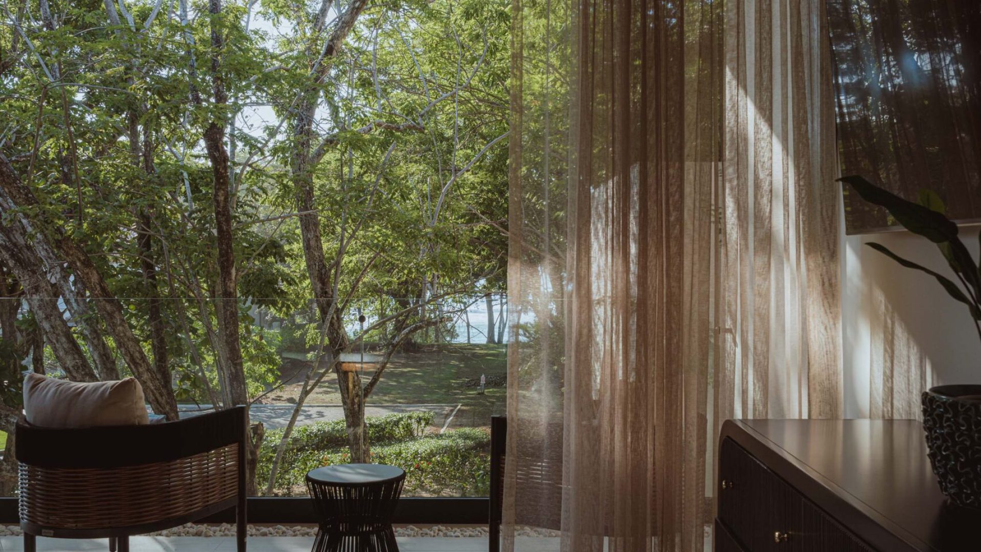 Cozy interior with large window overlooking lush green trees, natural light, modern furniture, wooden accents, calming residential space.