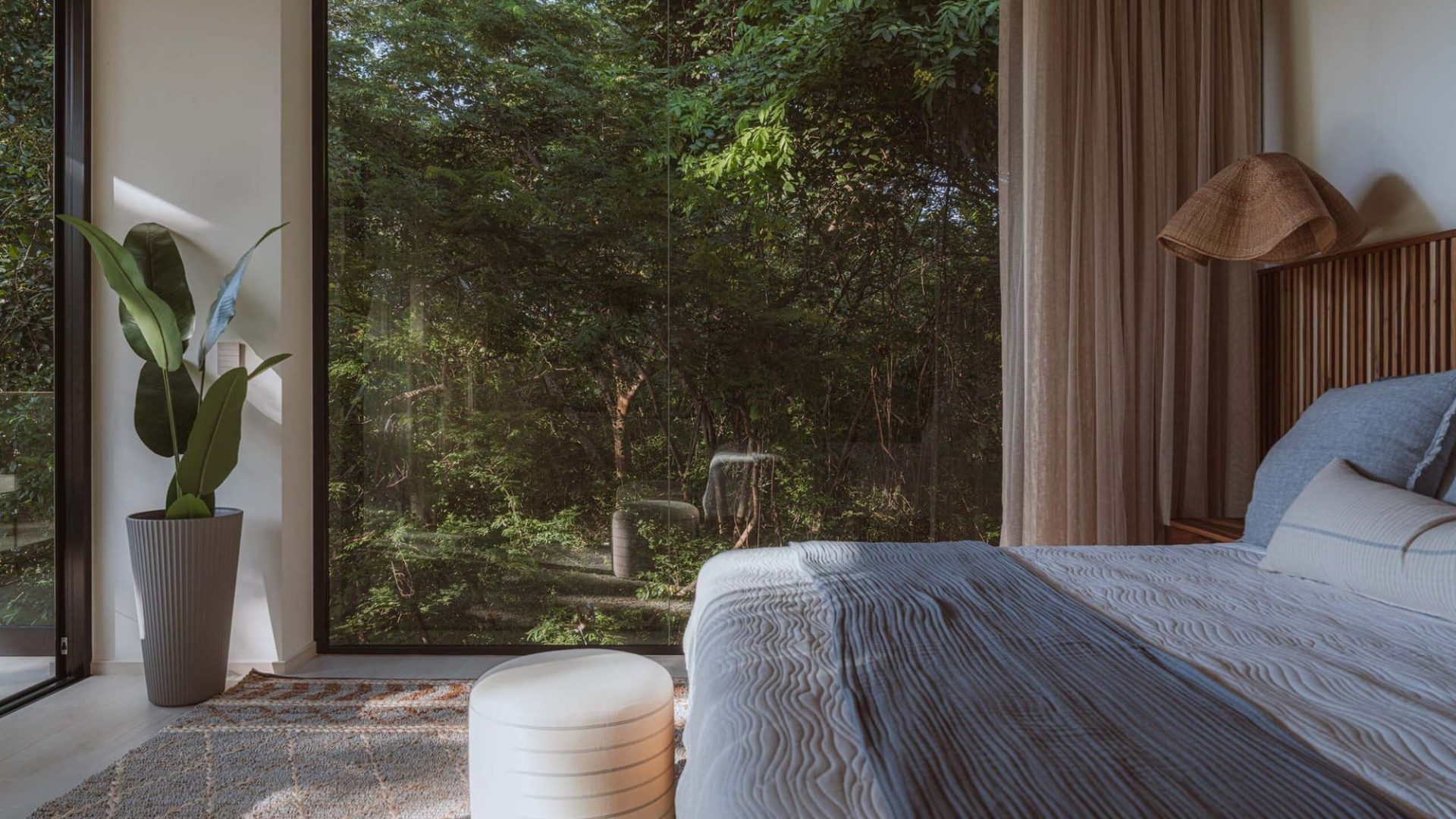 Serene bedroom with large window overlooking lush greenery, modern decor, and natural light.