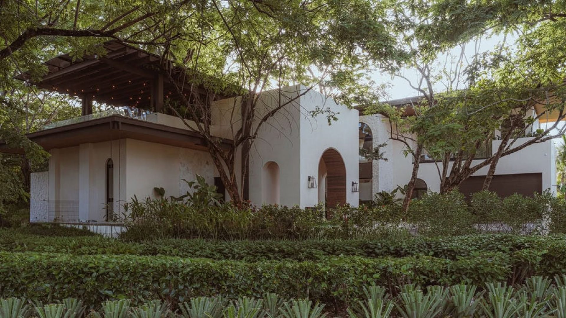 Modern white house with lush greenery and trees, stylish architecture, and outdoor living space.