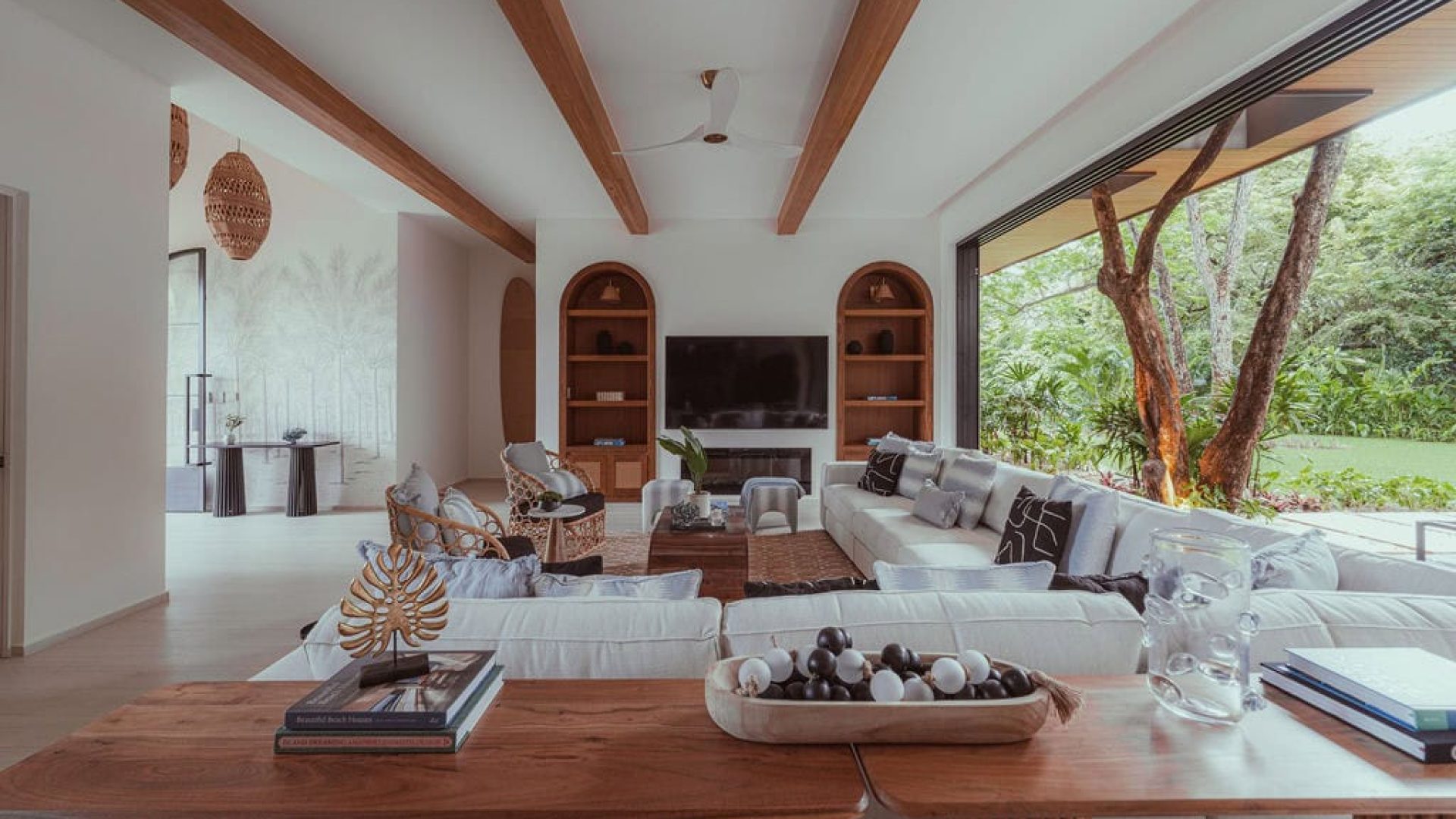Modern living room with open design, natural wood accents, and large windows overlooking lush greenery.
