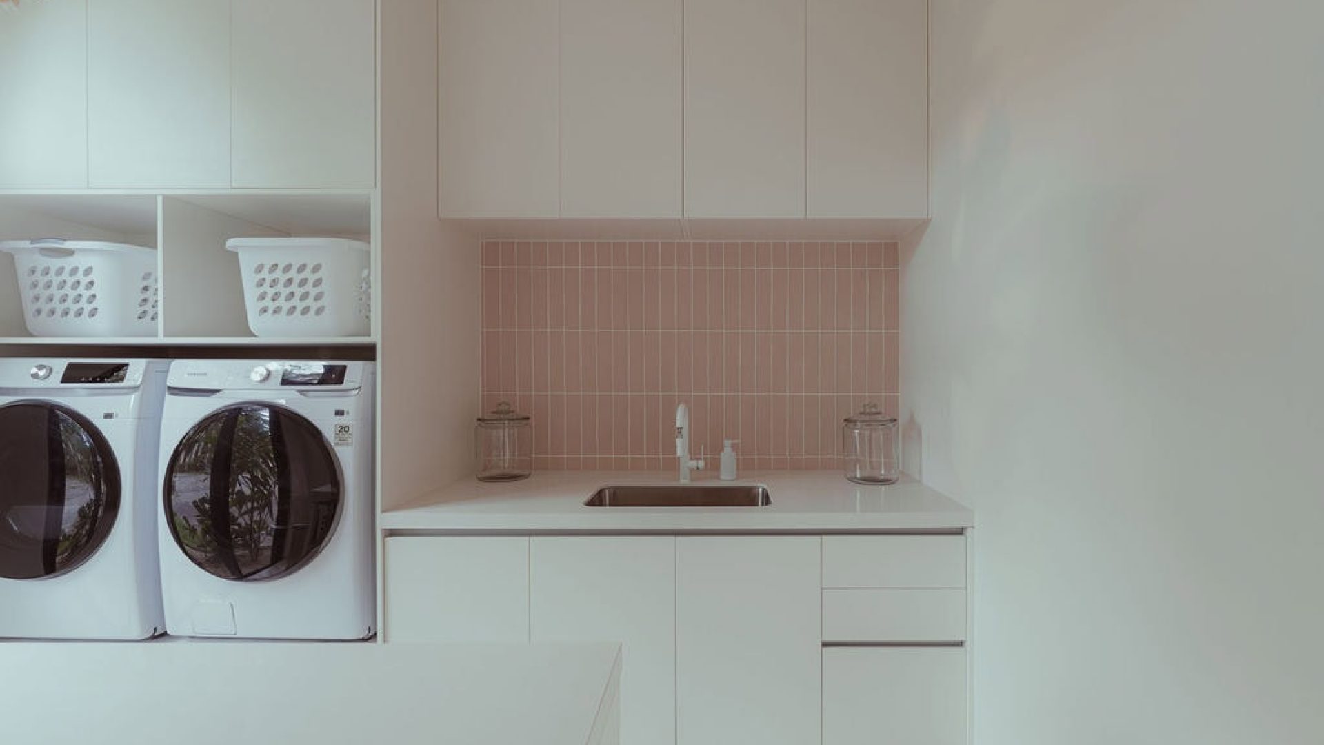 Bright laundry room with white cabinets and pink tiled backsplash in Vida Pinilla home.