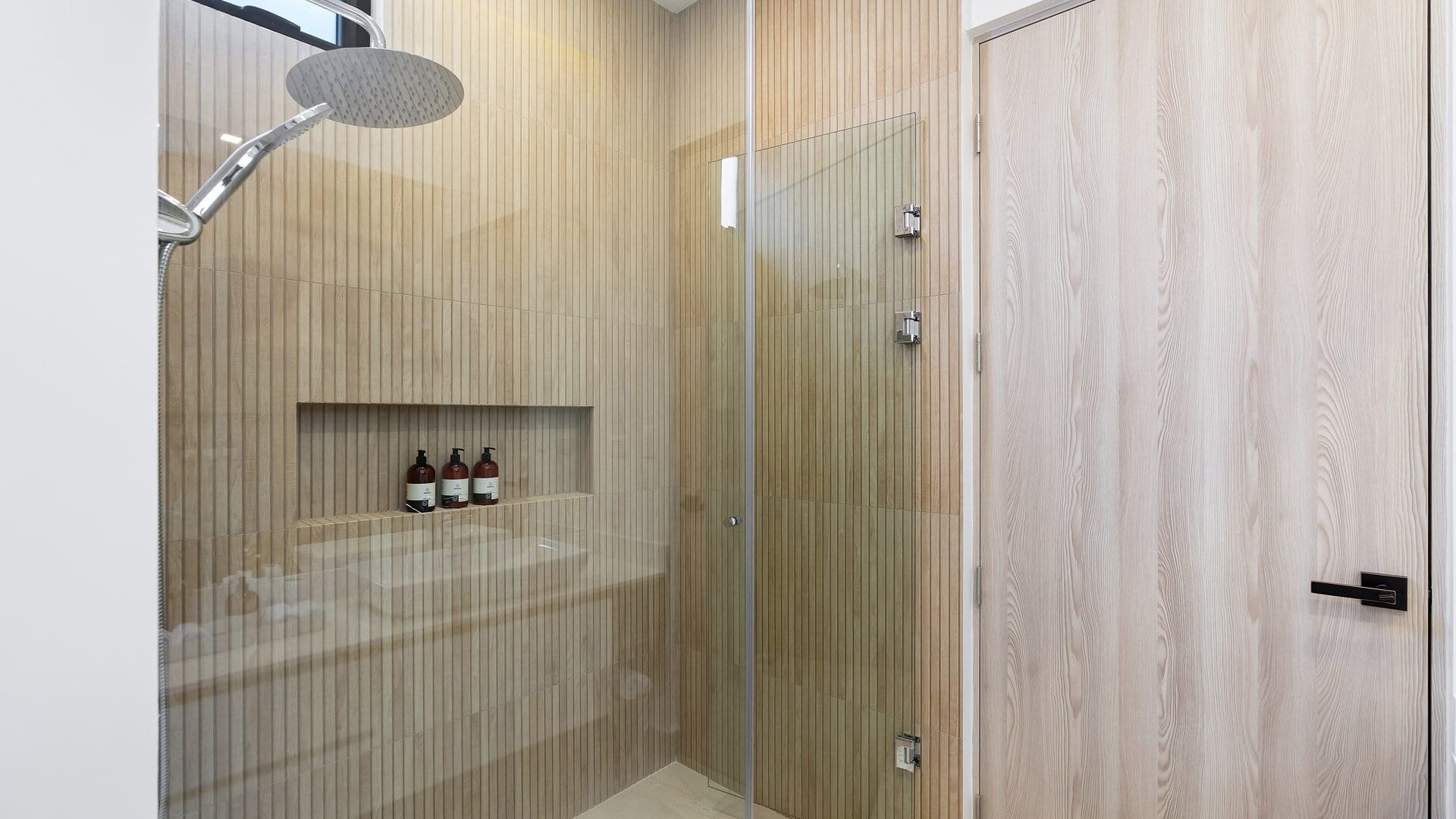 Sleek modern shower with wood-paneled walls and glass door, featuring shampoo bottles and rainfall showerhead.