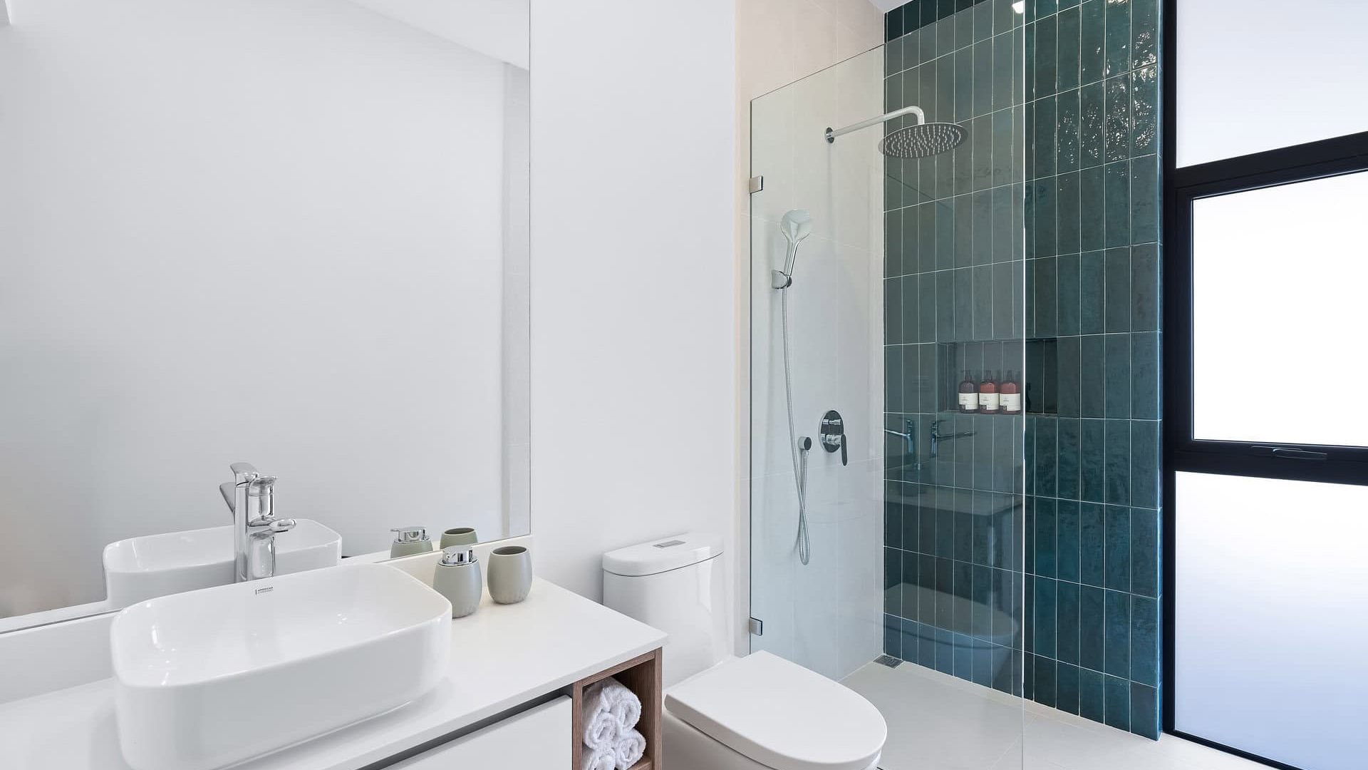 Modern minimalist bathroom with walk-in shower, white vanity, and green tiled wall, bright natural light.