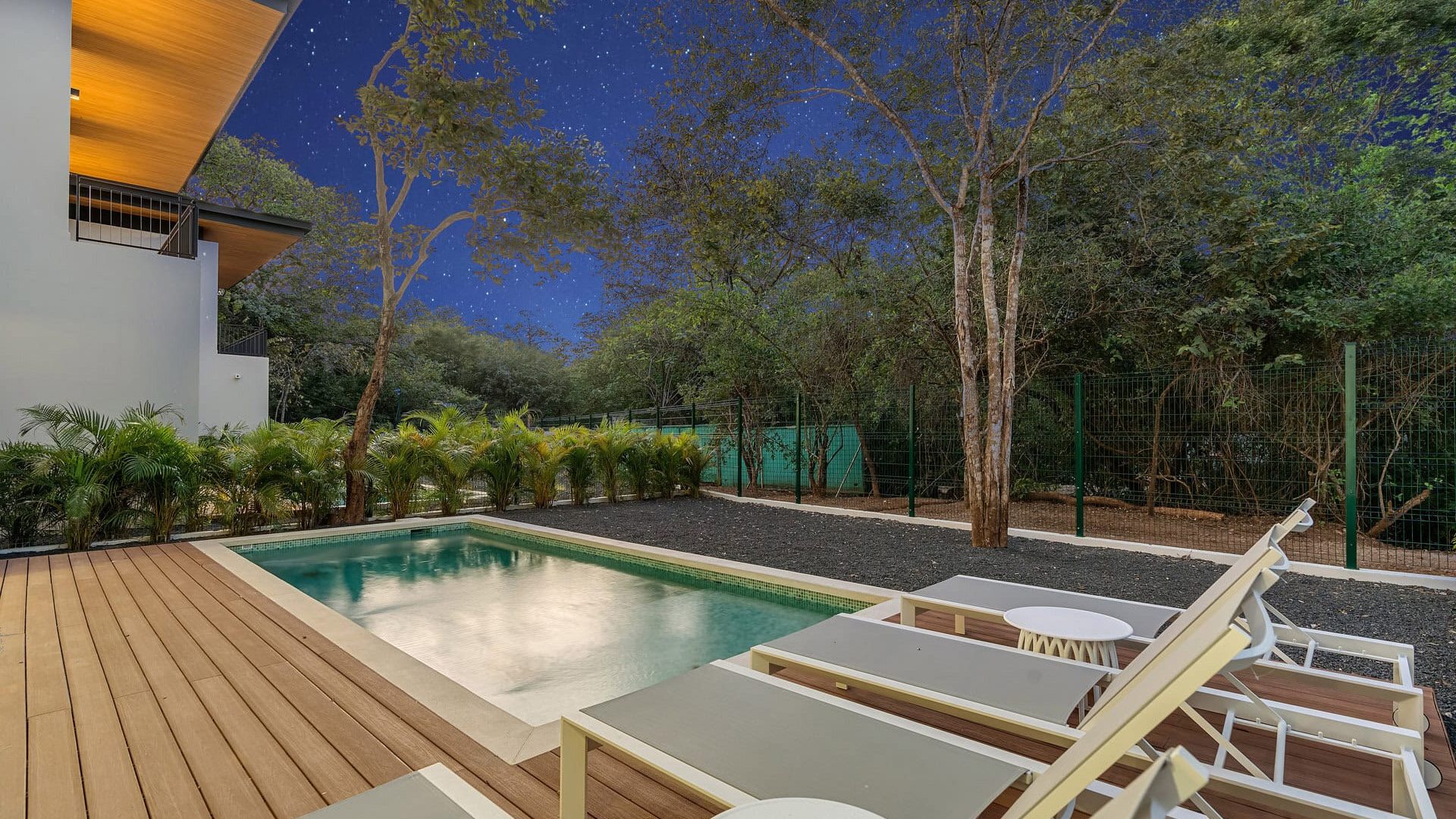 Modern backyard with swimming pool and outdoor lounge chairs under a starry night sky in Vida Pinilla.