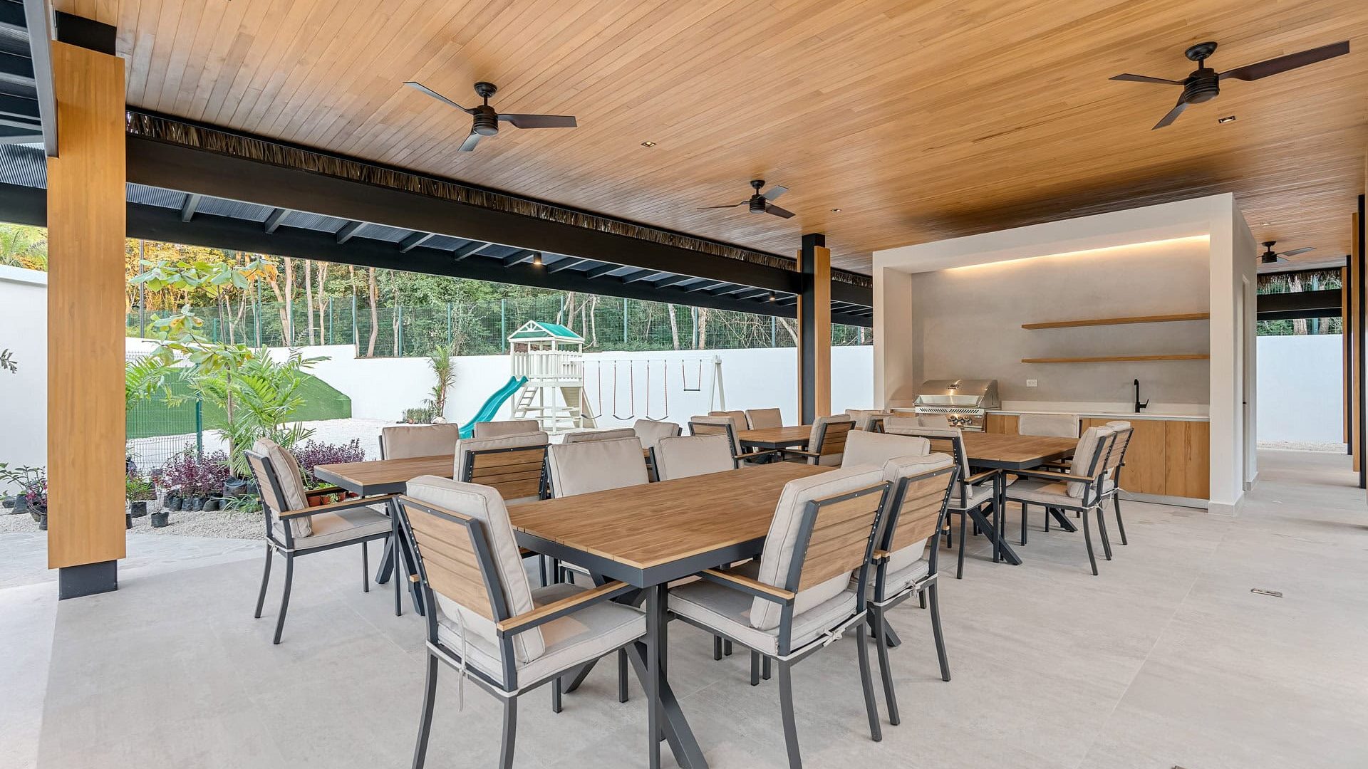 Modern outdoor dining area with wooden ceiling and ceiling fans at Vida Pinilla estate, featuring a barbecue station and shaded patio space.