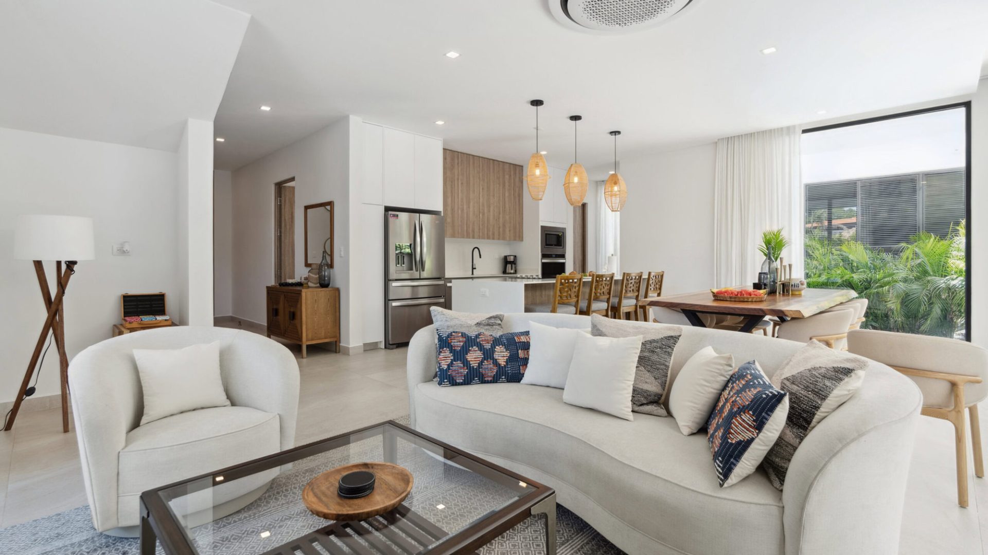 Modern living room with open kitchen, stylish furniture, and large window with greenery - Vida Pinilla.