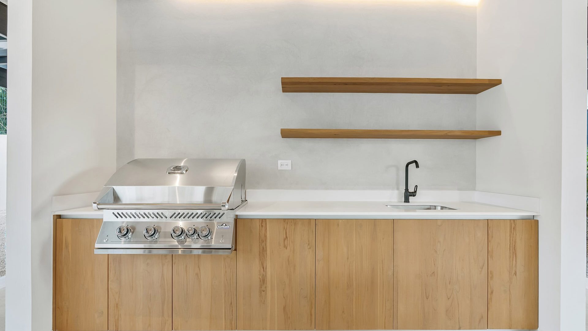 Modern outdoor kitchen with stainless steel grill, wooden cabinets, and minimalist design.