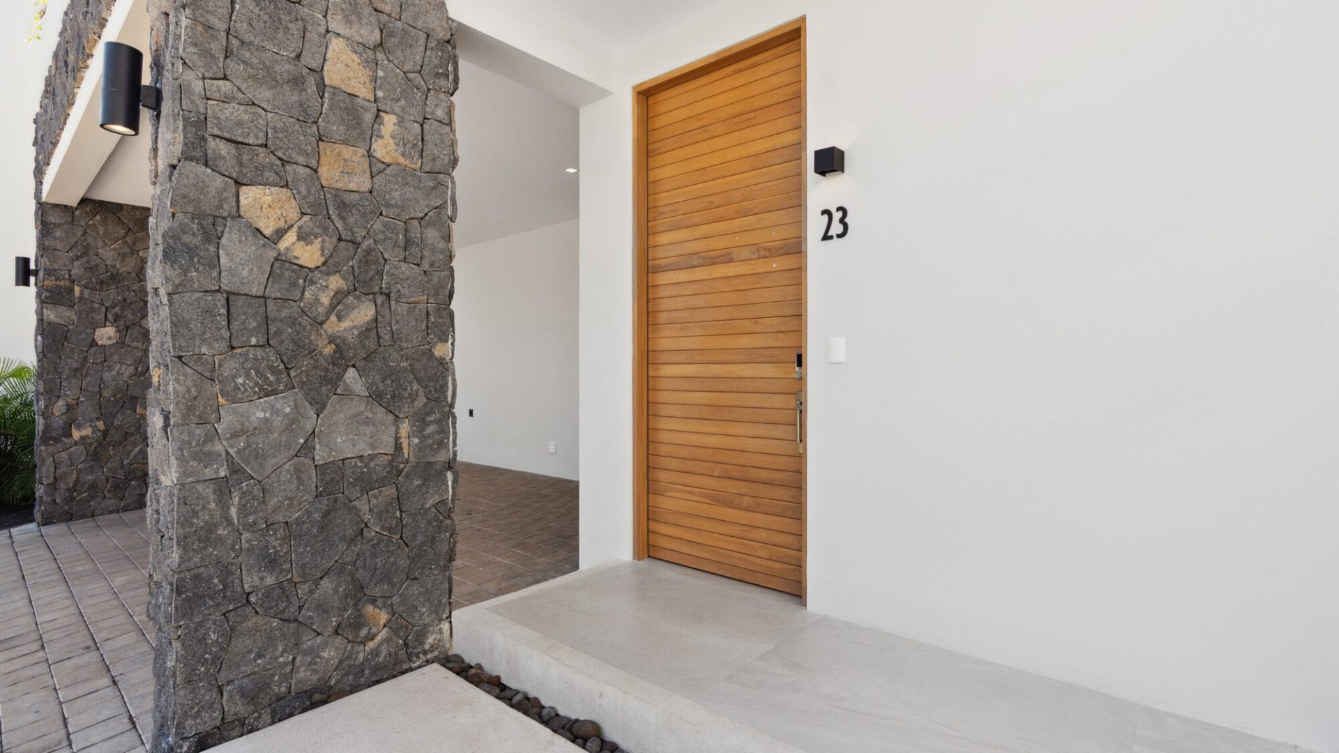 Elegant modern house entrance with stone wall accents and wooden door, featuring minimalist design and clean white walls.