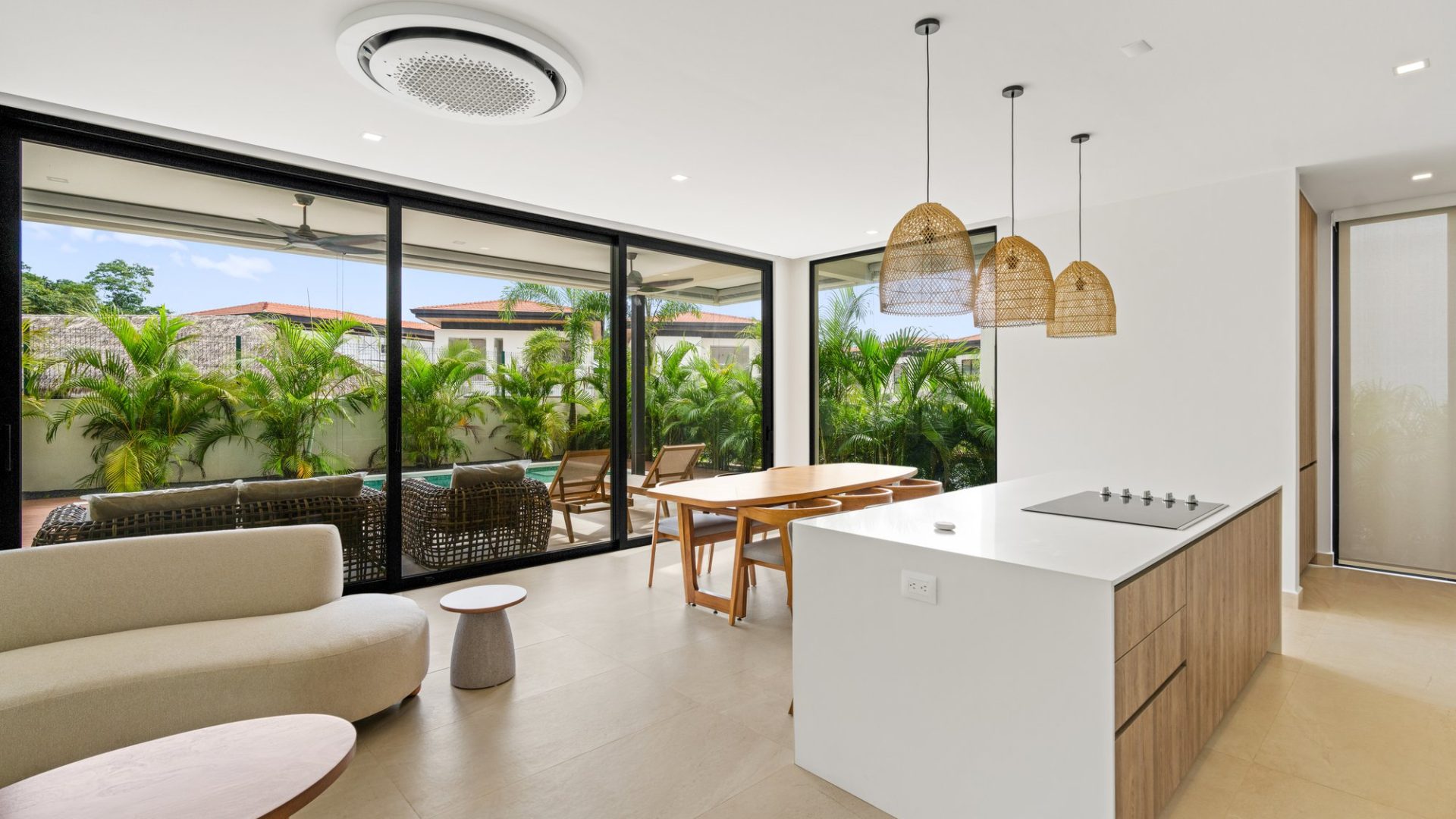 Modern open-plan kitchen and living area with large glass doors and lush greenery outside.