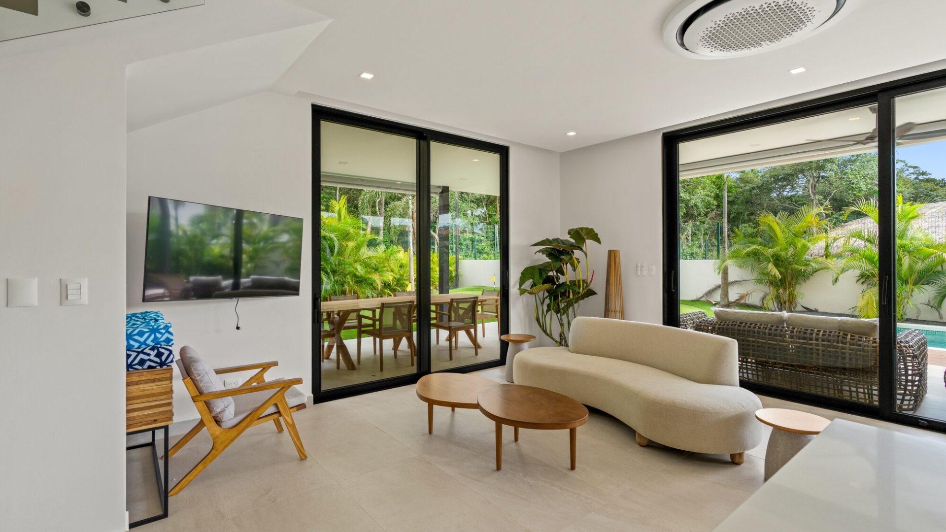Modern living room with large glass sliding doors, tropical outdoor seating, and contemporary furniture.
