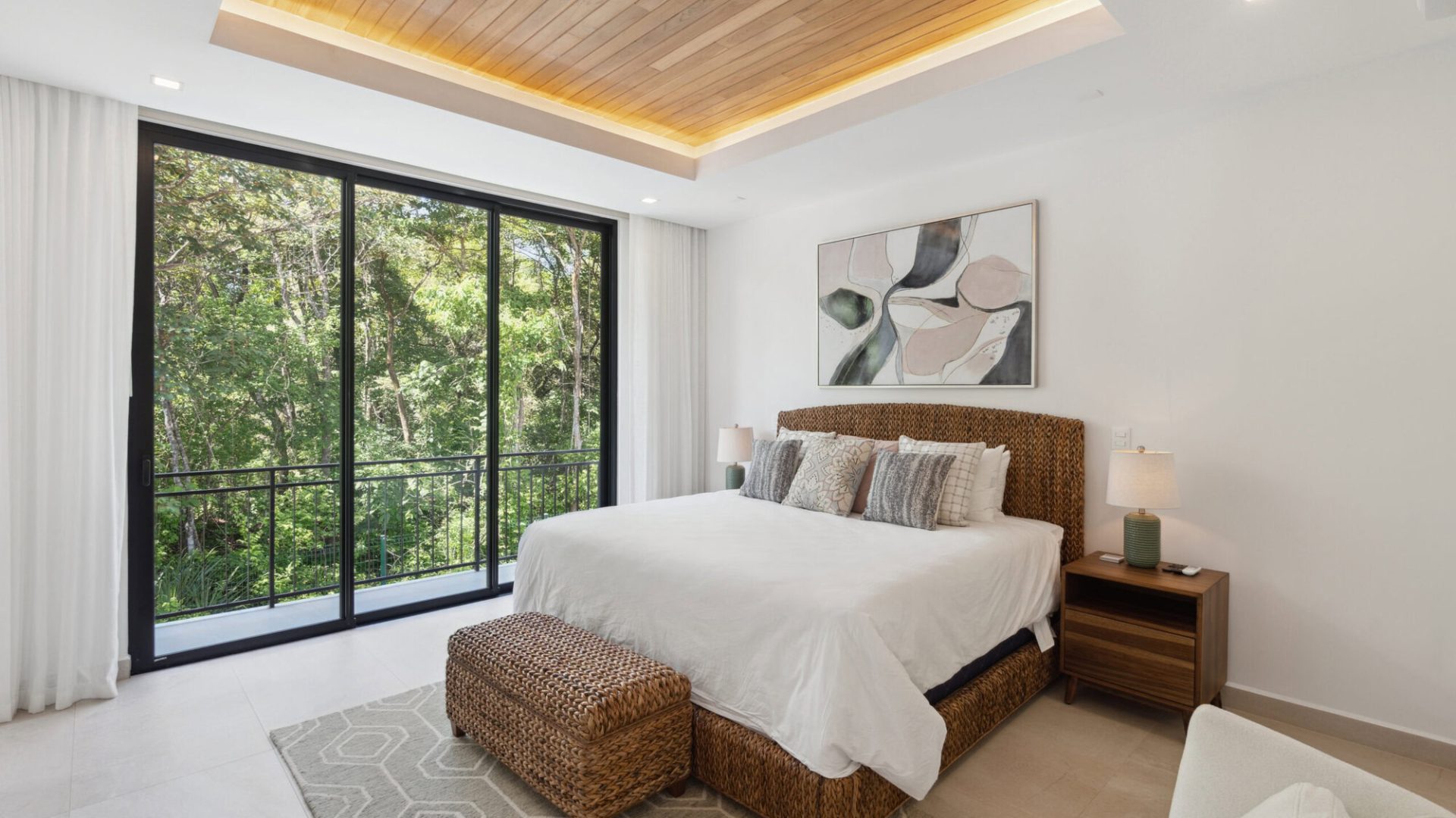 Bright bedroom with large sliding glass doors overlooking lush green trees, modern decor, and natural wood accents.