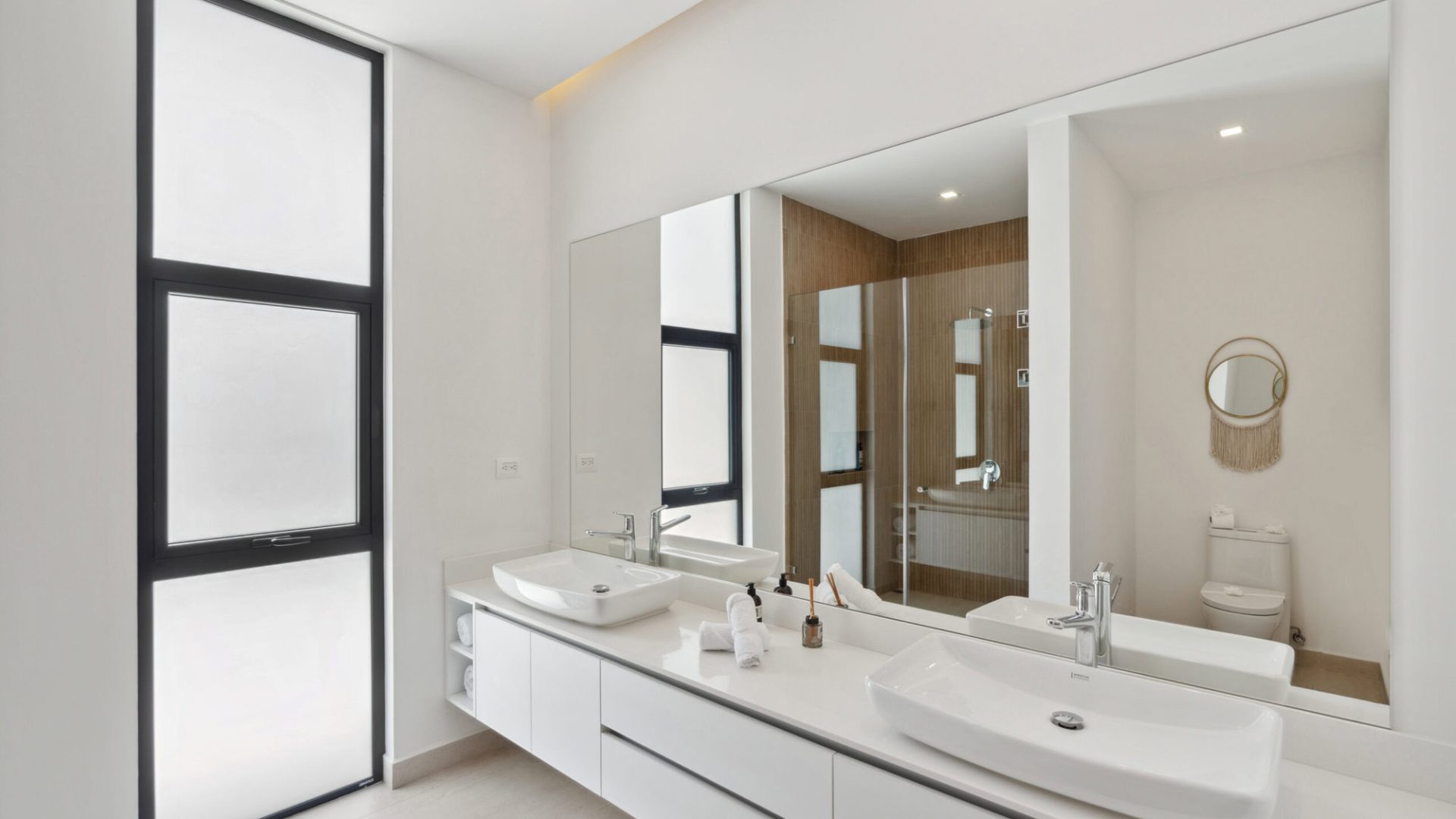 Modern minimalist bathroom with double sinks, large mirror, and natural lighting.