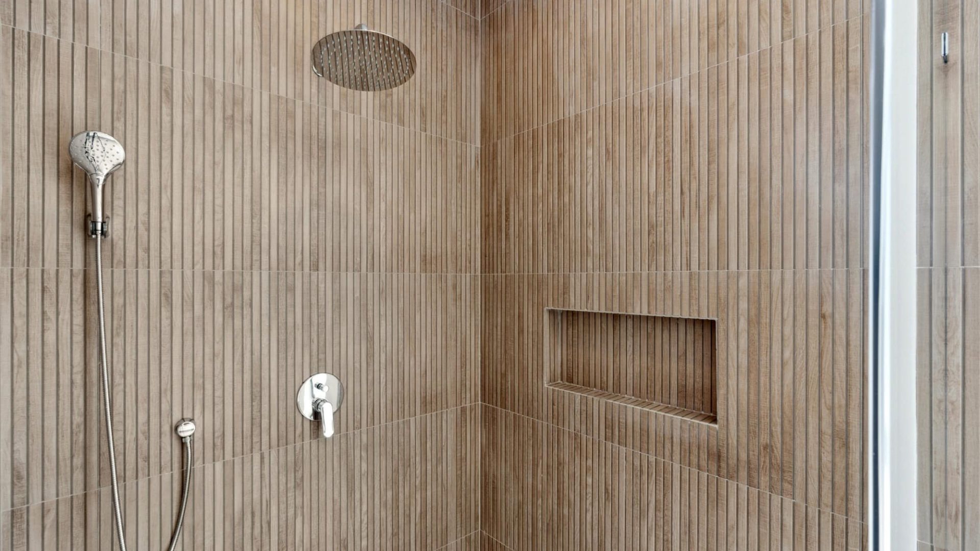 Modern walk-in shower with wooden tile walls, recessed shelf, rain showerhead, and handheld sprayer for a luxurious bathroom experience.
