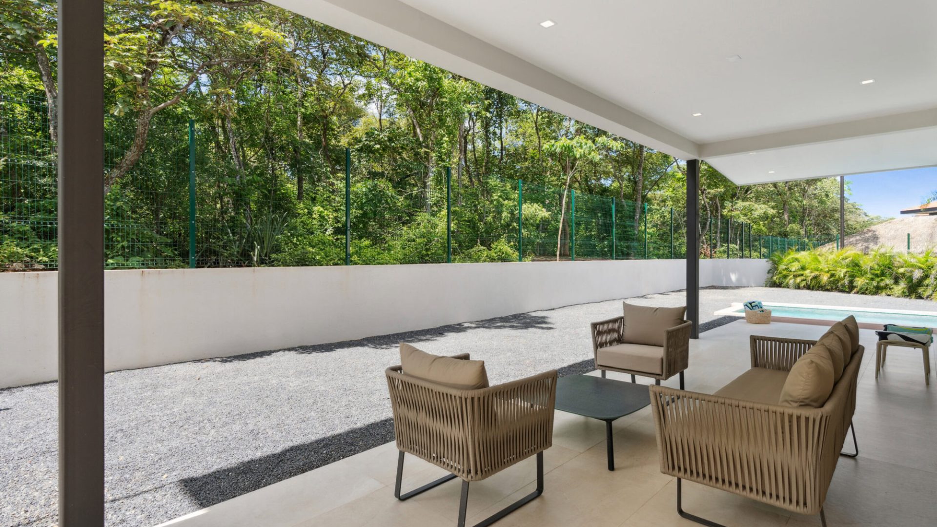 Spacious covered outdoor patio with modern furniture and view of lush greenery.