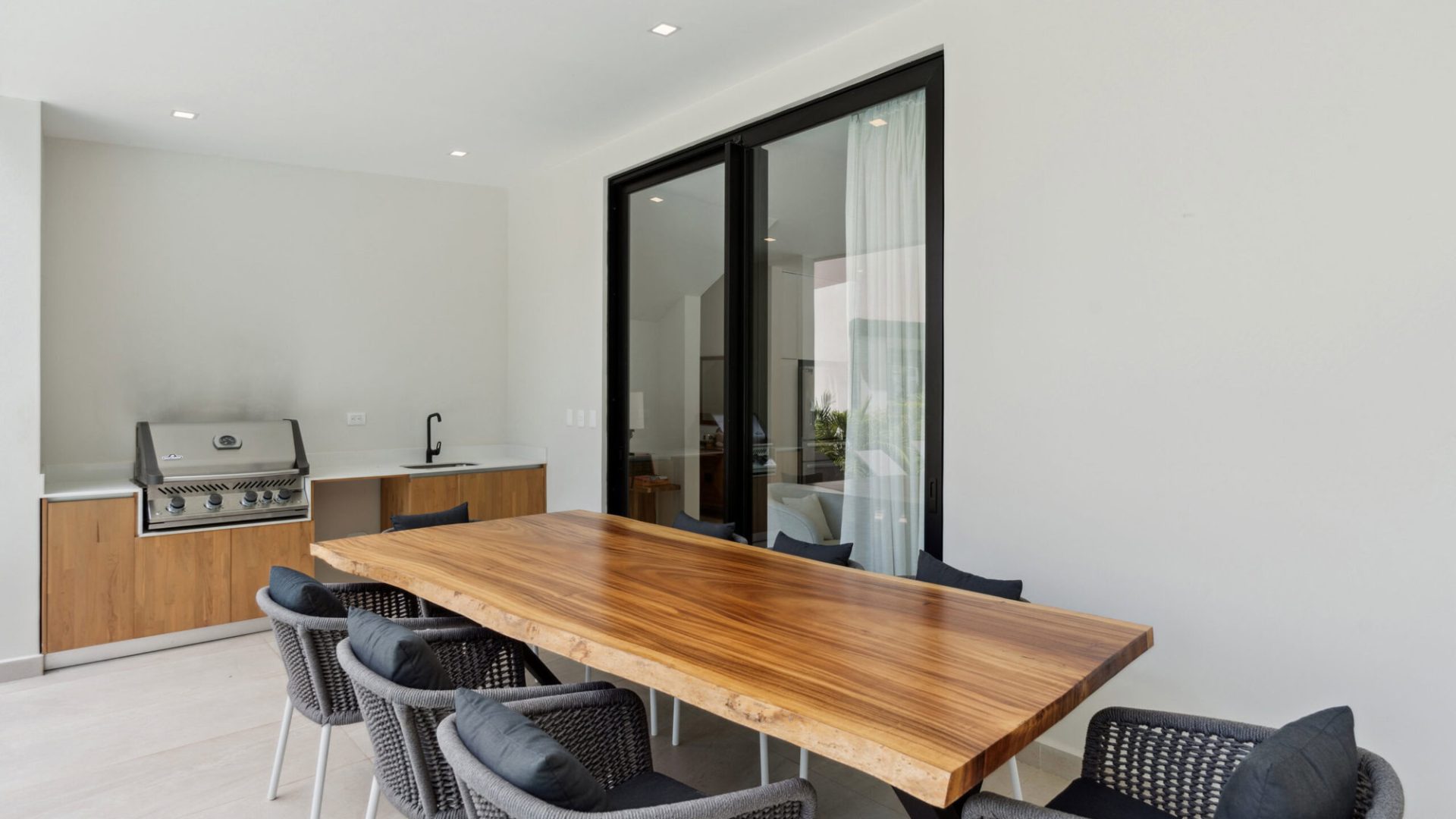 Modern dining area with outdoor kitchen, black-framed sliding glass doors, and minimalist decor for upscale home living.