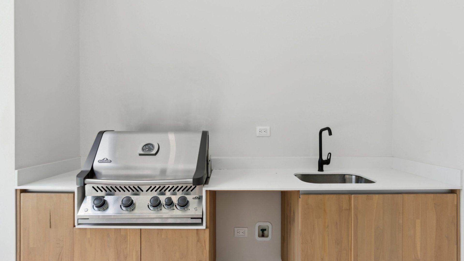 Modern kitchen with wooden cabinets, stainless steel grill, and black faucet.