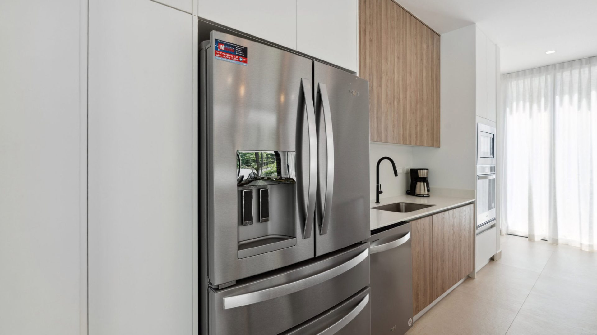 Stainless steel refrigerator in a modern kitchen with wooden and white cabinetry.