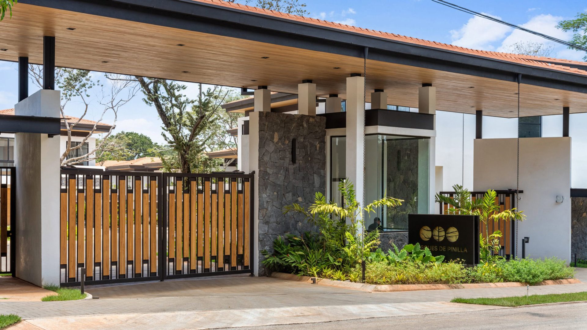 Modern residential entrance with wooden fence and lush greenery, showcasing contemporary architecture.