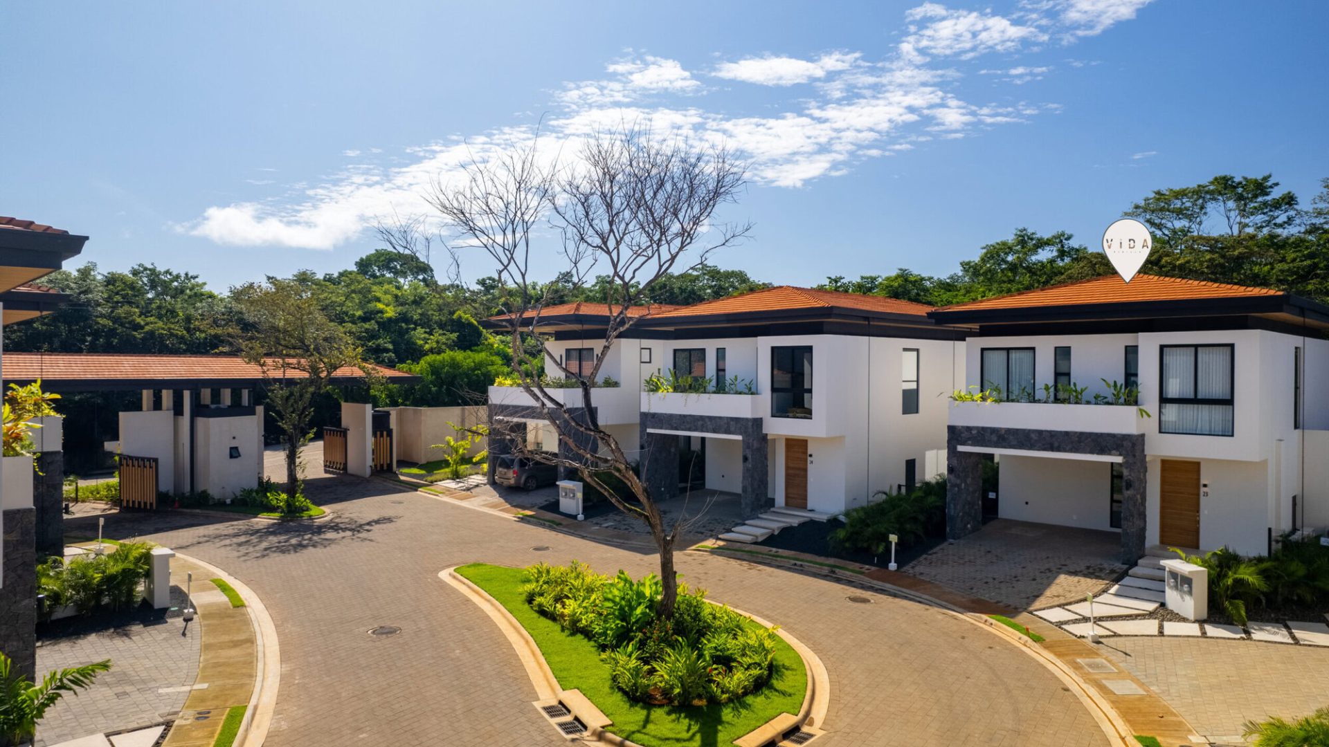 Modern residential houses in a gated community with lush landscaping and clear blue skies.