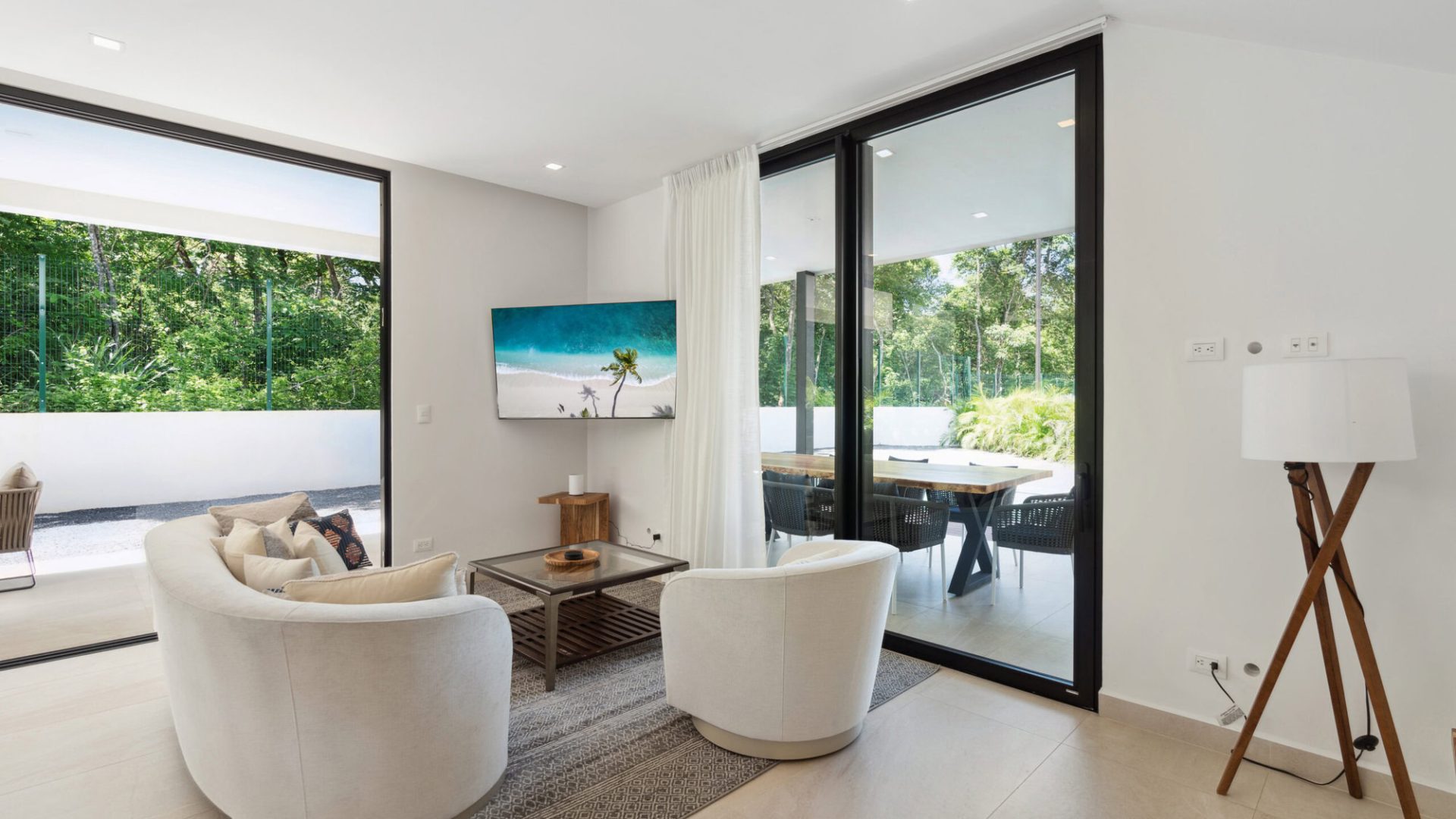 Modern living room with large glass doors and natural light, overlooking lush green outdoor space.