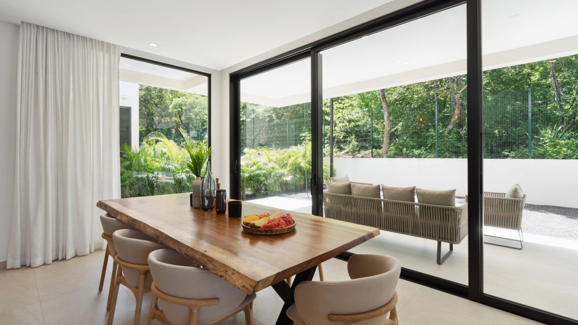 Contemporary dining room with large glass sliding doors opening to outdoor patio and lush greenery.