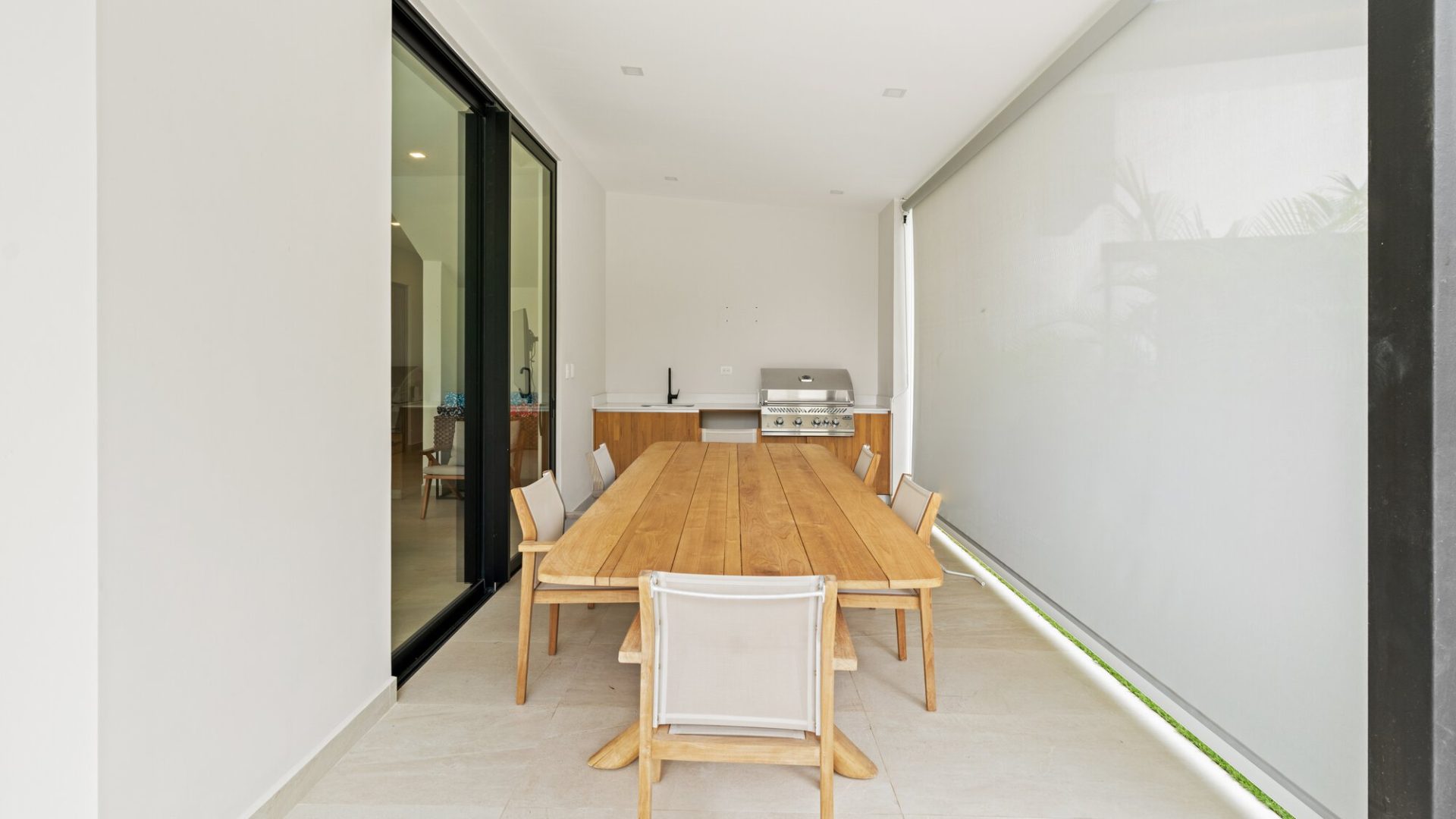 Outdoor dining area with wooden table and chairs near a modern kitchen, bright and airy patio space.