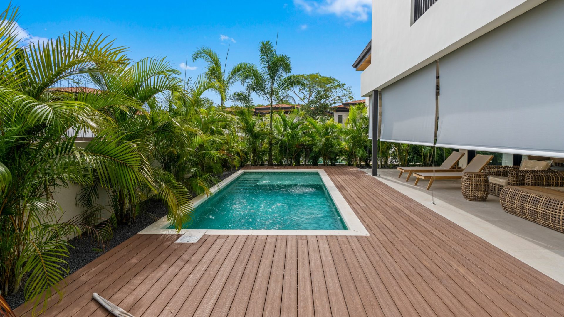 Lush tropical plants surround a modern private pool on a wooden deck.
