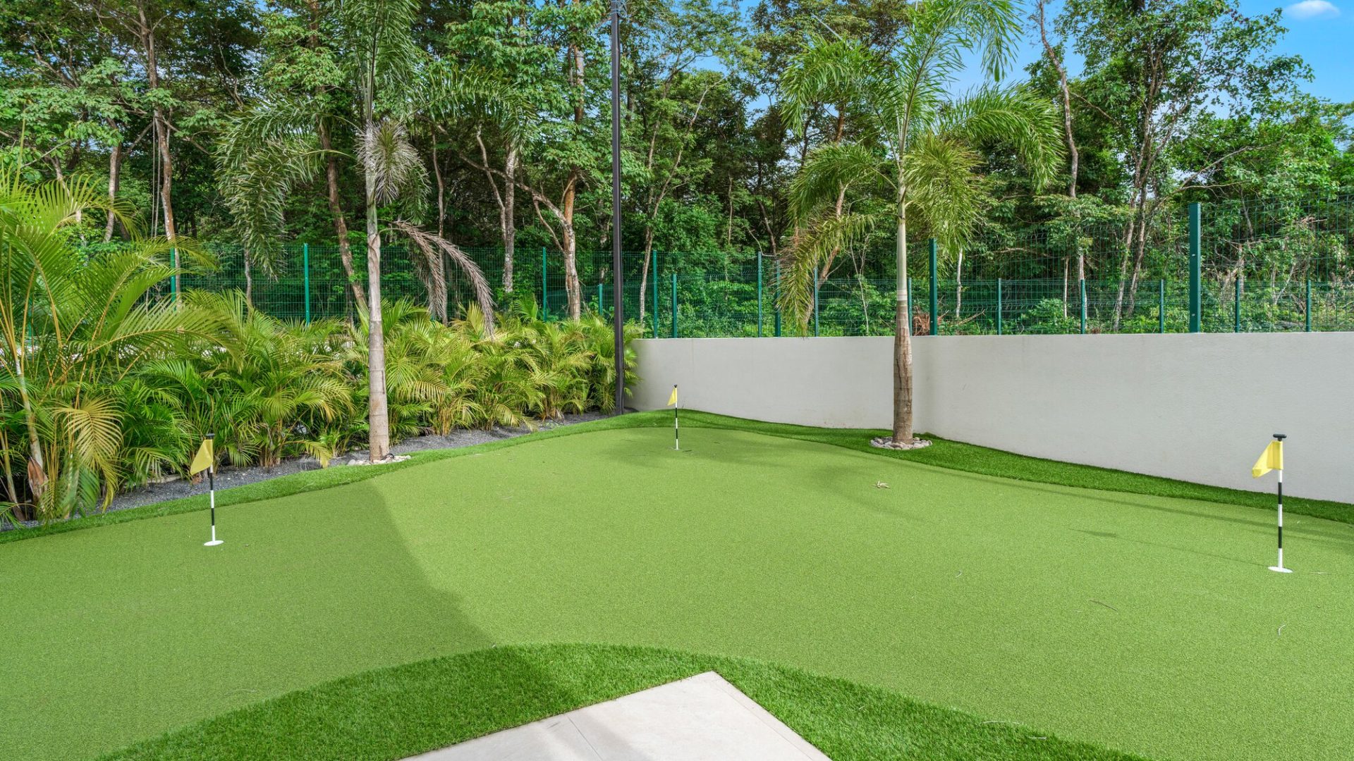 Lush outdoor mini golf course with putting green, surrounded by tropical plants and trees.