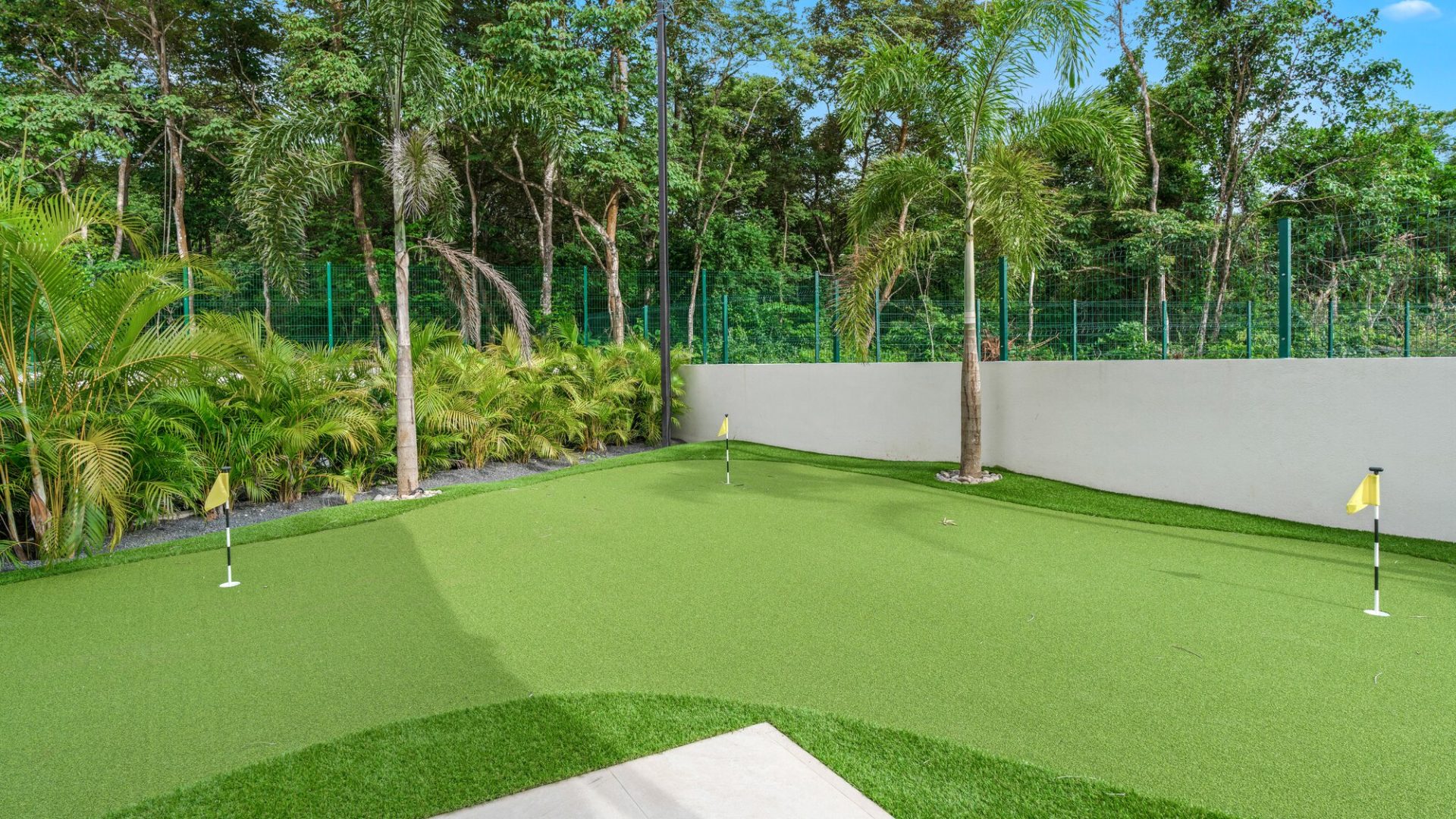 Lush backyard putting green surrounded by tropical plants and trees for outdoor golf practice.