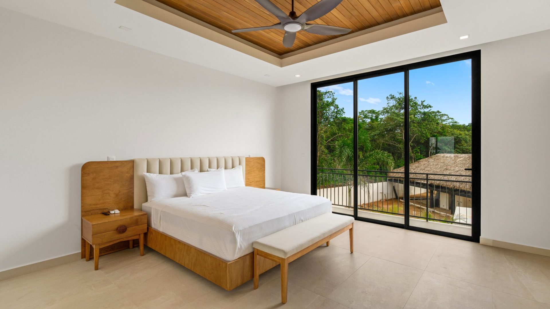 Bright modern bedroom with large glass sliding doors overlooking lush greenery and tropical scenery.