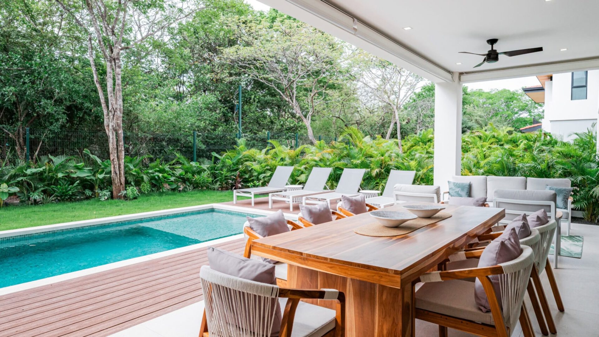 Modern outdoor dining area with pool and lush greenery, perfect for relaxing and entertaining.