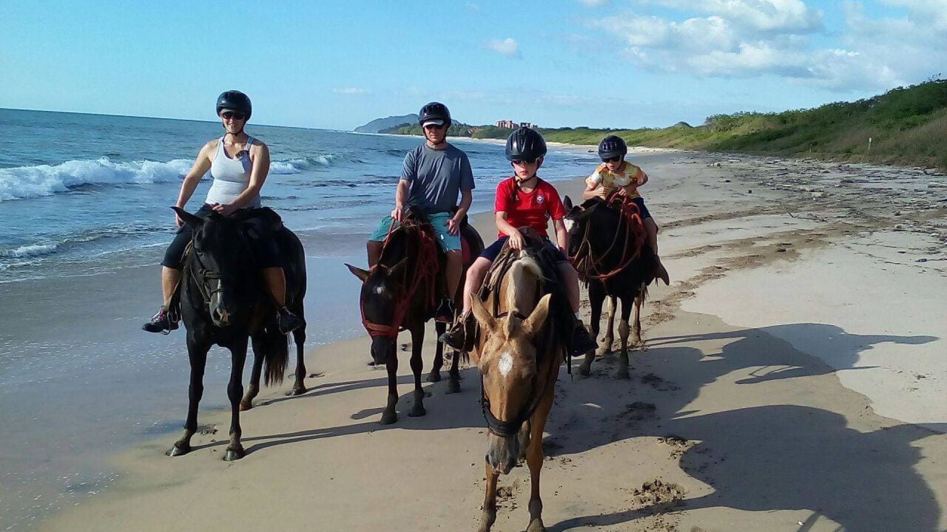Horseback riding on the beach with a group of people enjoying a sunny day.