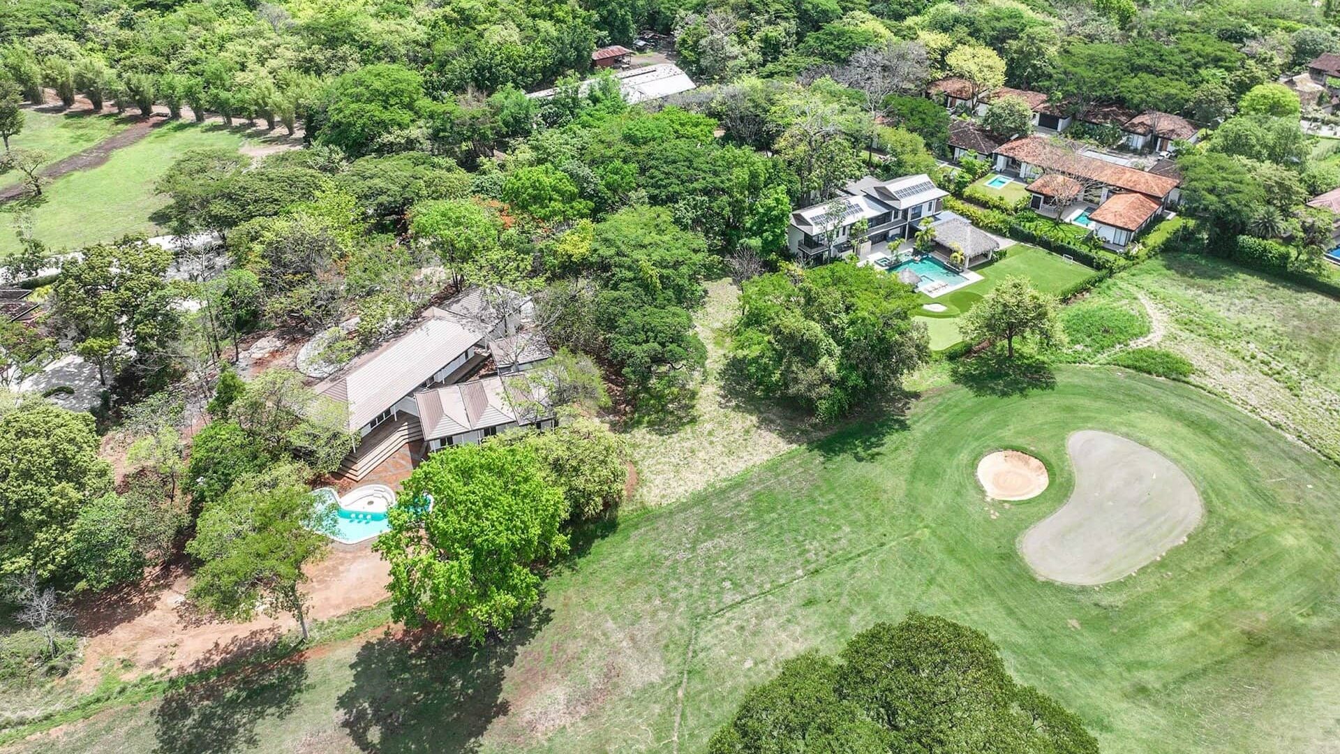 Lush green residential area with golf course and swimming pools, surrounded by trees.
