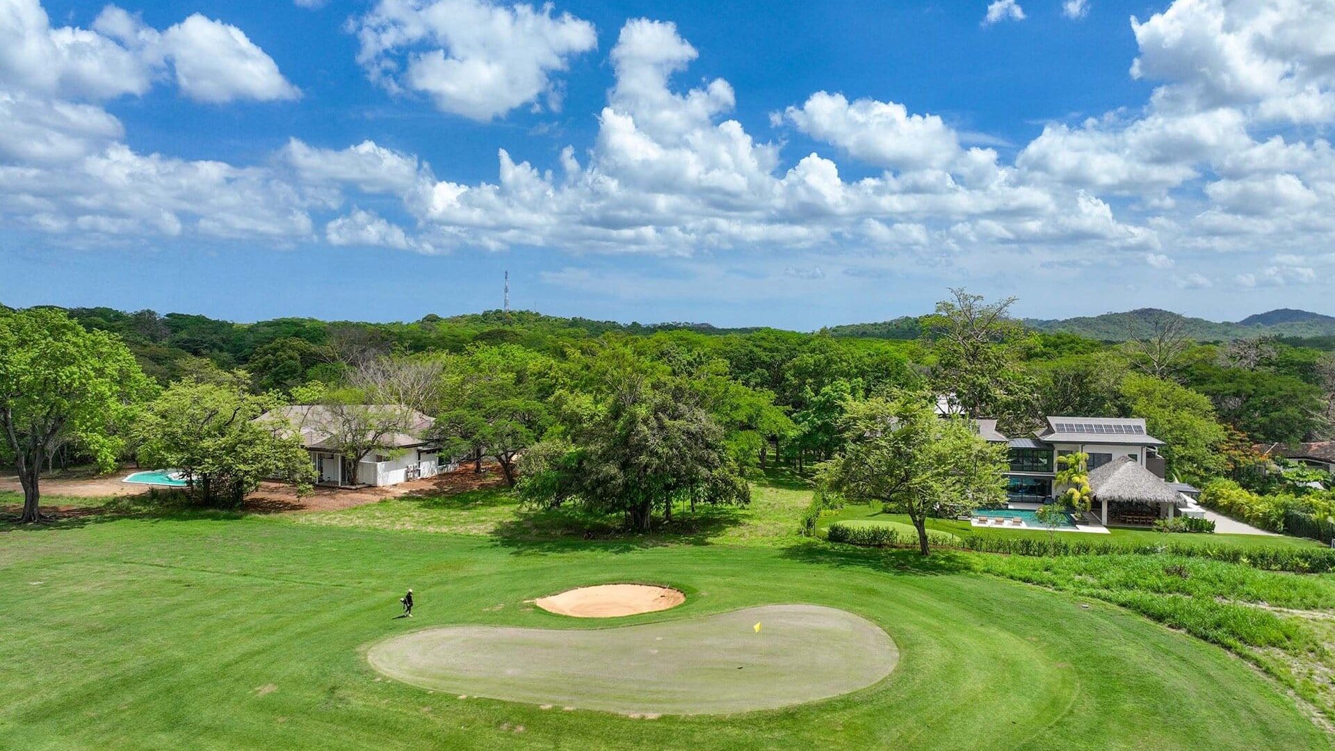 Lush golf course with modern house and scenic mountain view under clear blue sky.