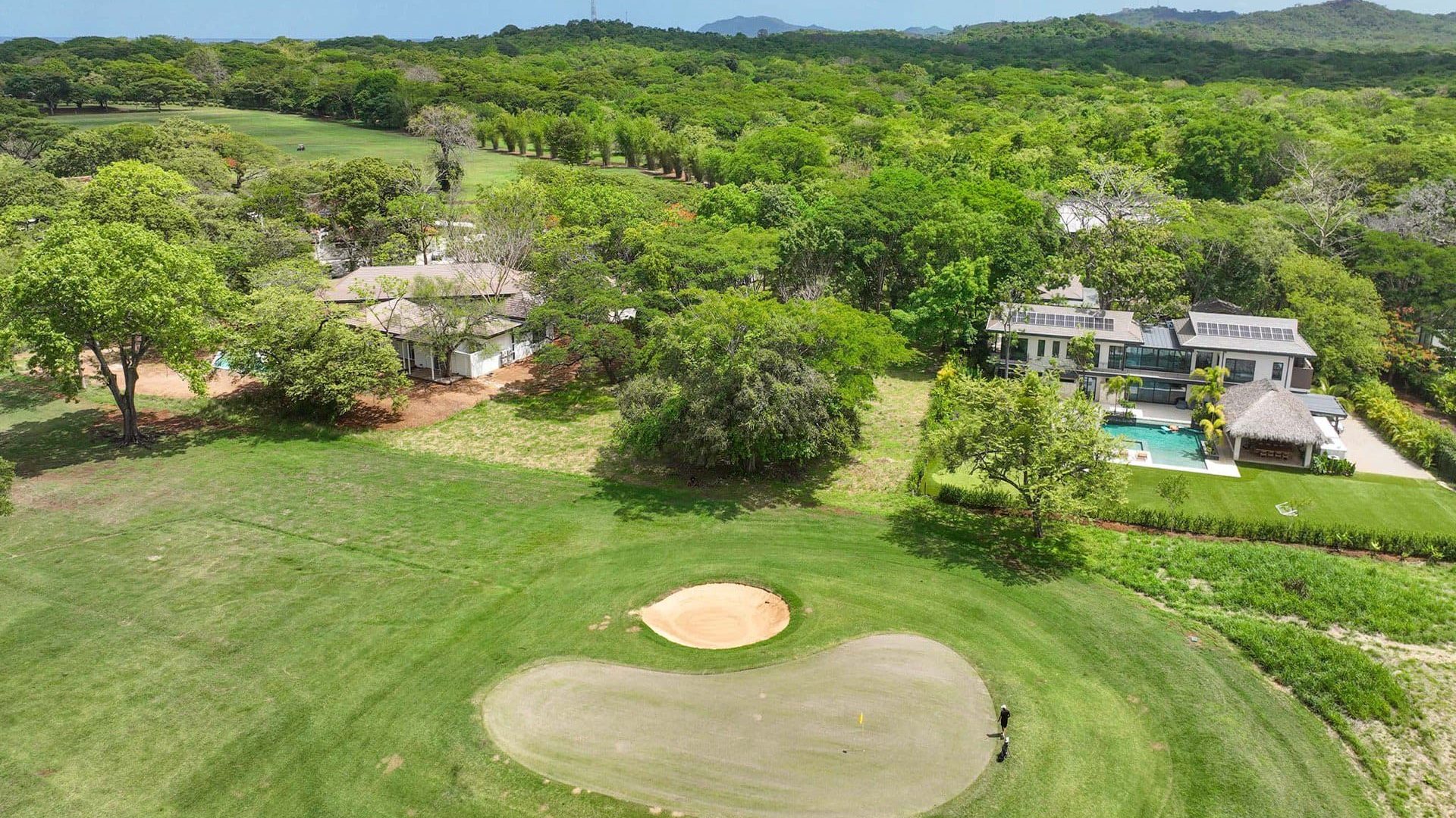 Lush golf course and luxurious modern villa with swimming pool surrounded by greenery and trees.