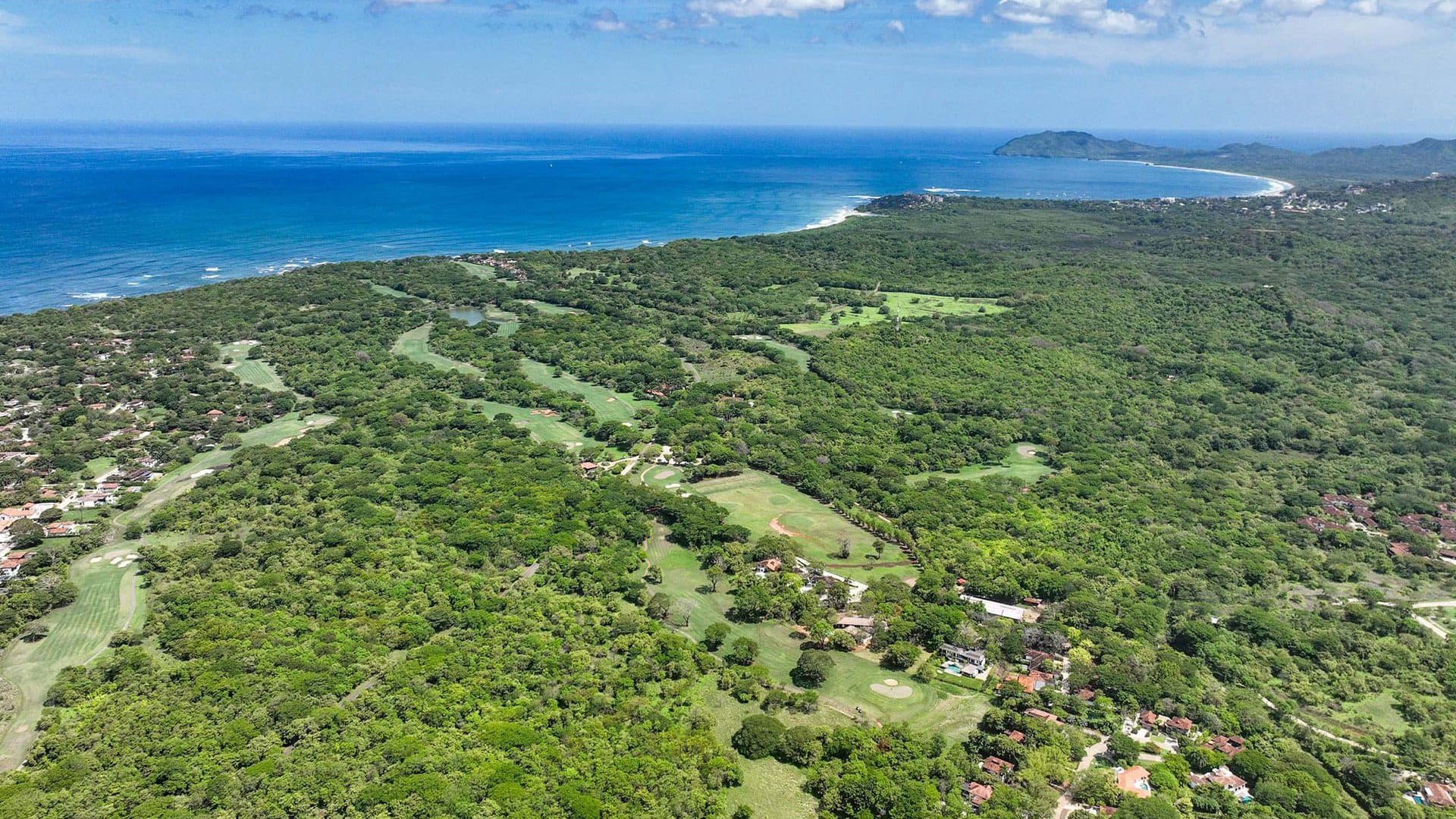 Vivid aerial view of a lush green golf course near the coast with ocean in the background.