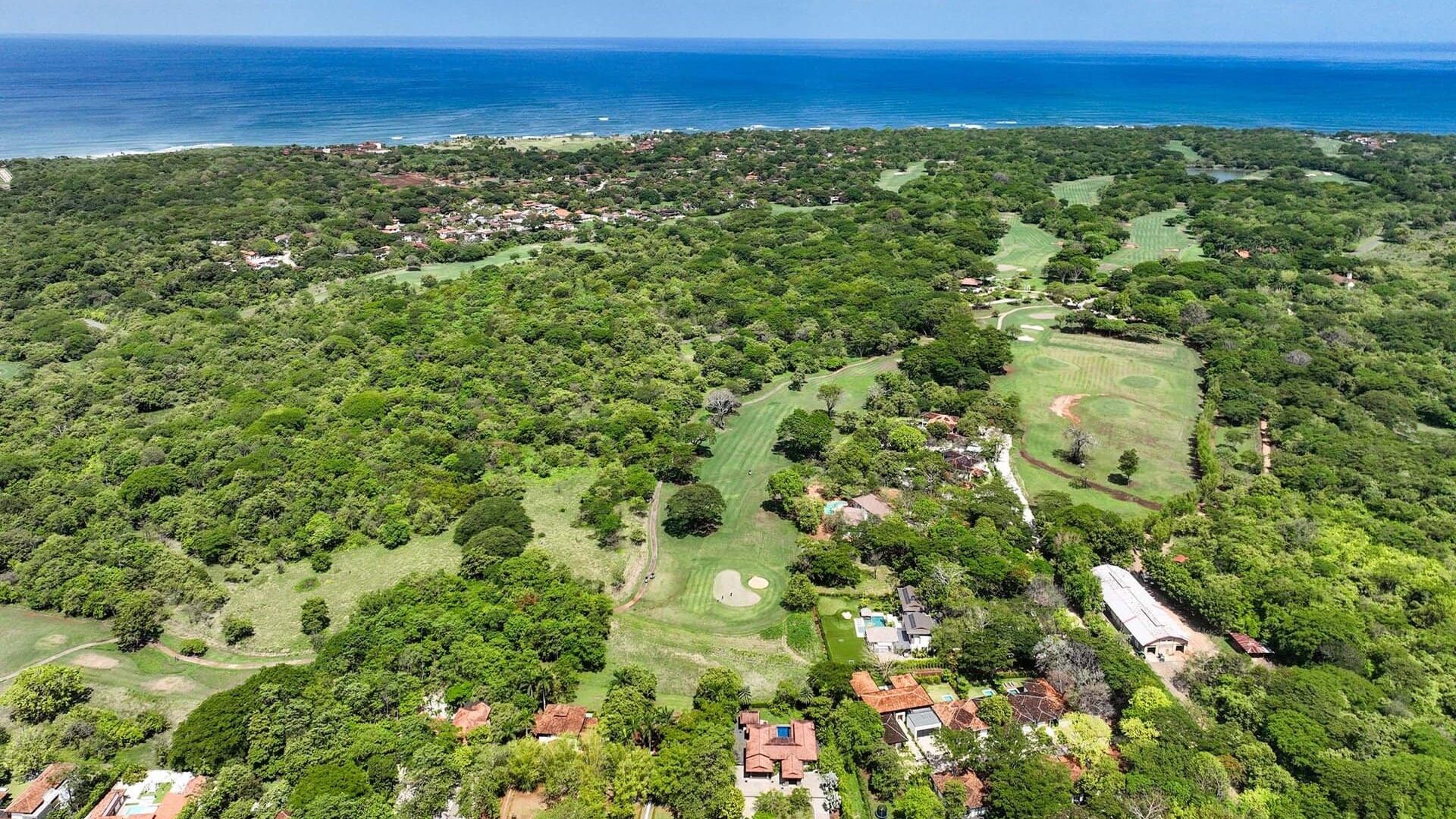 Lush green golf course and residential area near the coast with ocean view.