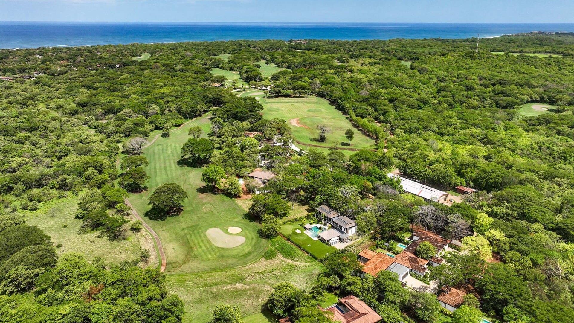 Lush golf course with ocean view surrounded by greenery and residential homes.