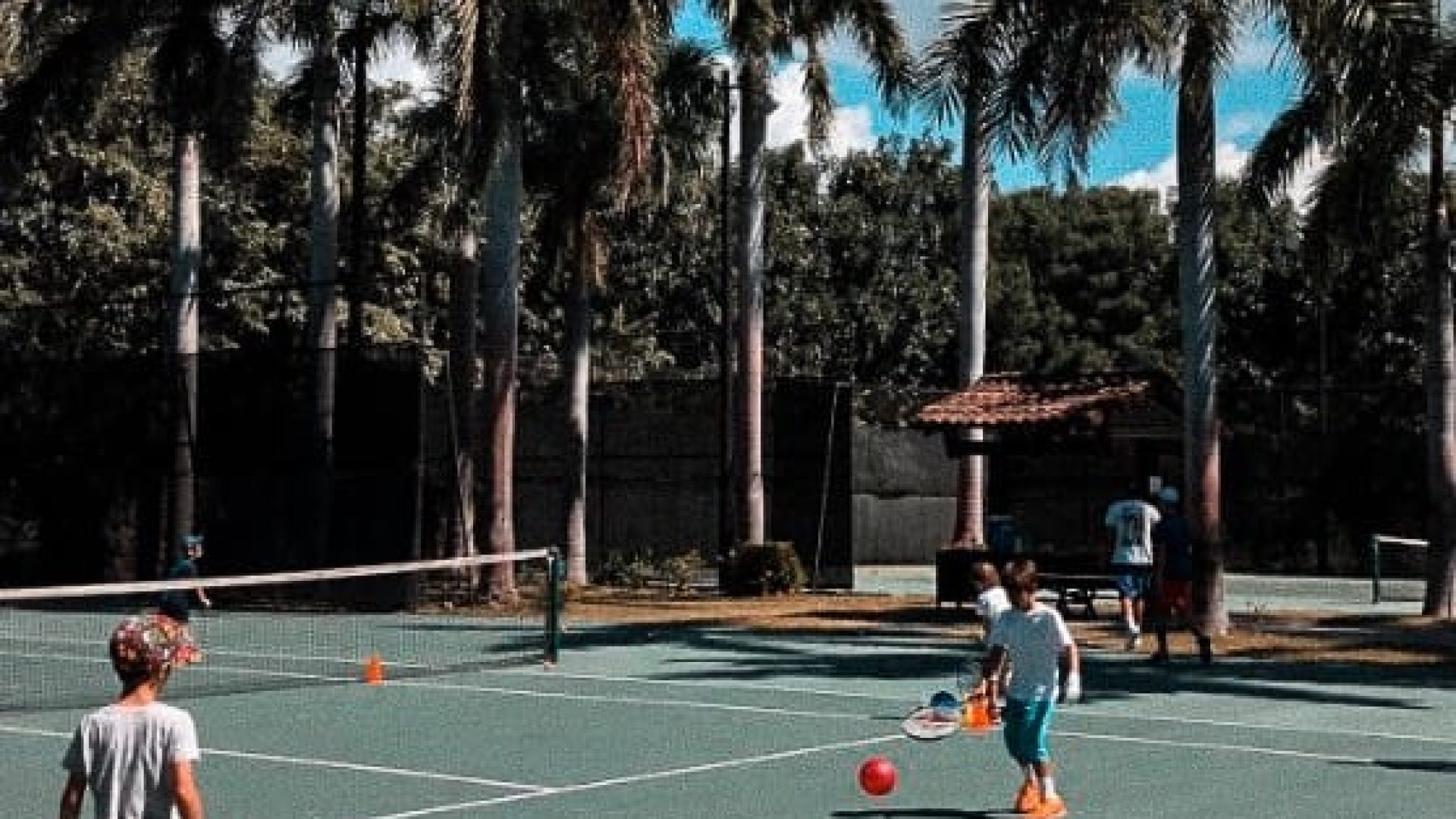 Kids playing tennis outdoors on a sunny day at Vida Pinilla. Family-friendly sports facility with palm trees and vibrant atmosphere.