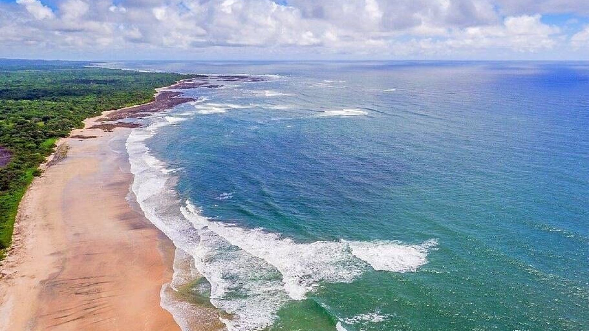 Serene coastal beach with clear blue water and lush green surroundings, perfect for relaxation.